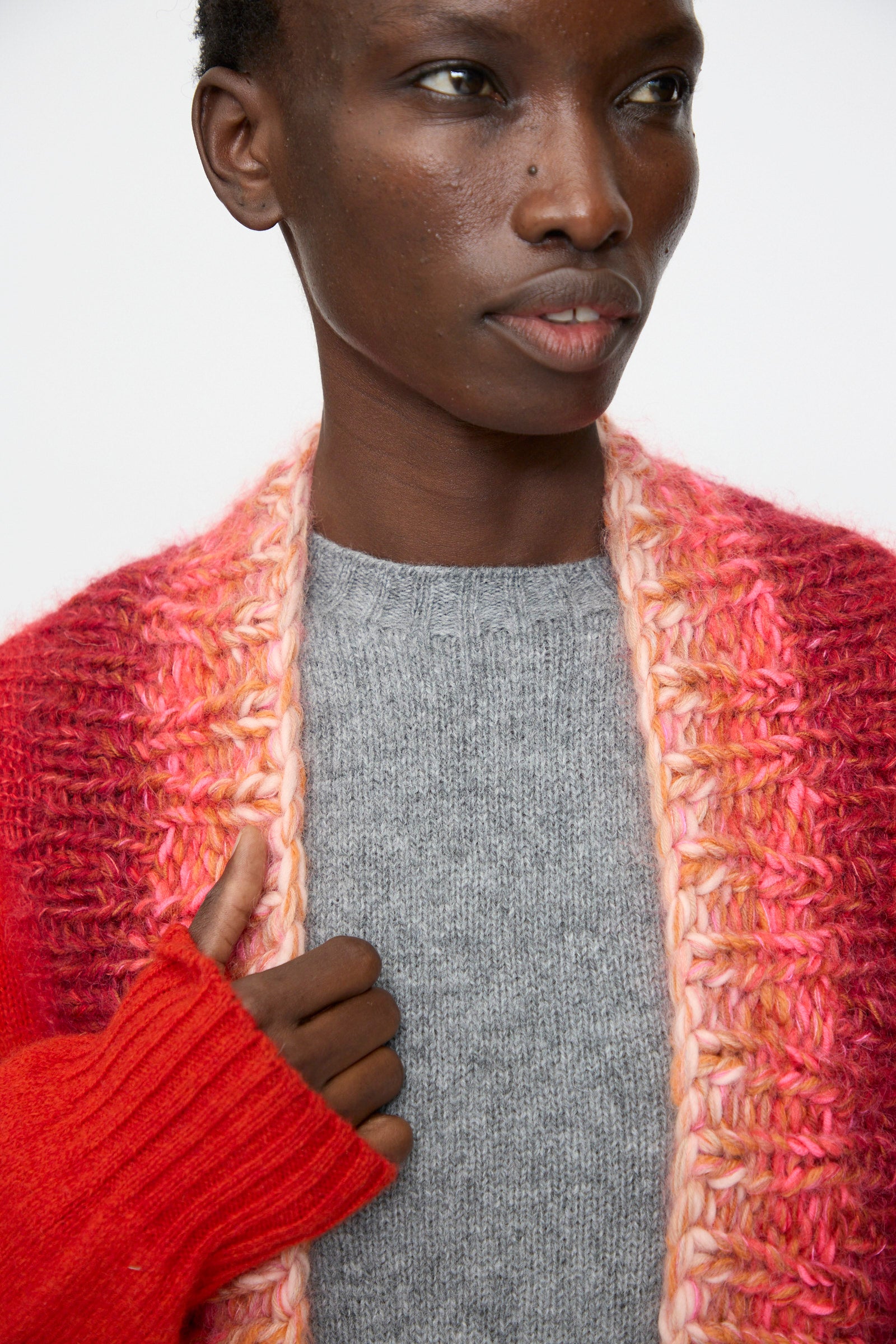 A person wears the Bless No. 70 Passencardigan in Scarlet, shown from the shoulders up against a plain background.