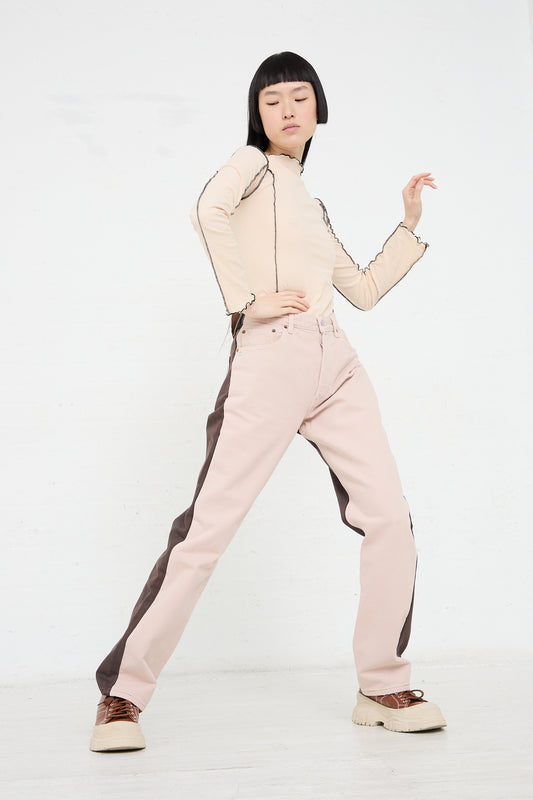 Woman posing in an up-cycled Bless No. 73 Jeanspleatfront in Pink/Brown outfit with one hand raised against a white background.