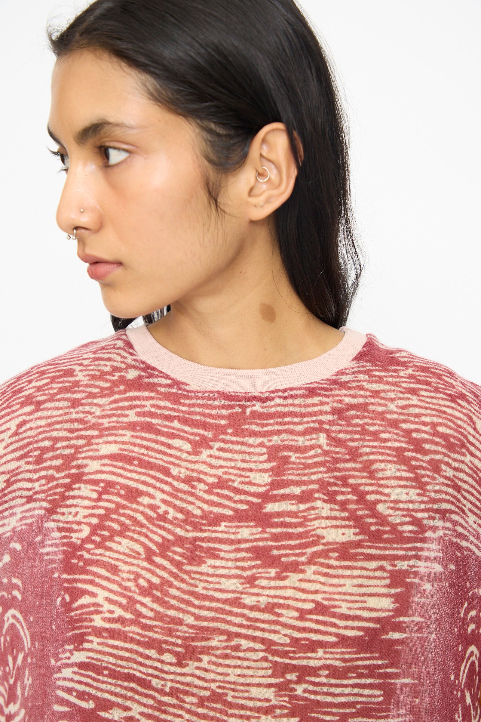 A person with long dark hair, wearing the Bless No. 81 M-Sweater in Exelephant, looks to the left. They have nose and ear piercings.