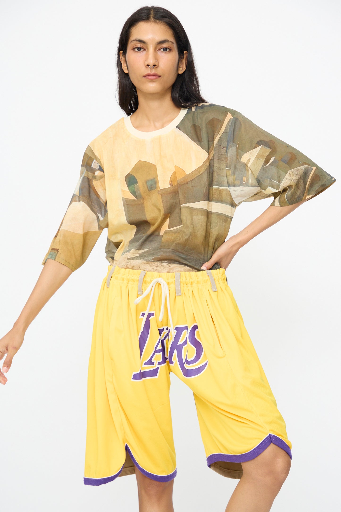 A person wearing a brown abstract print t-shirt and Bless No. 81 Overjoggingshorts in Vintage Basketball Unique II stands against a plain white background.