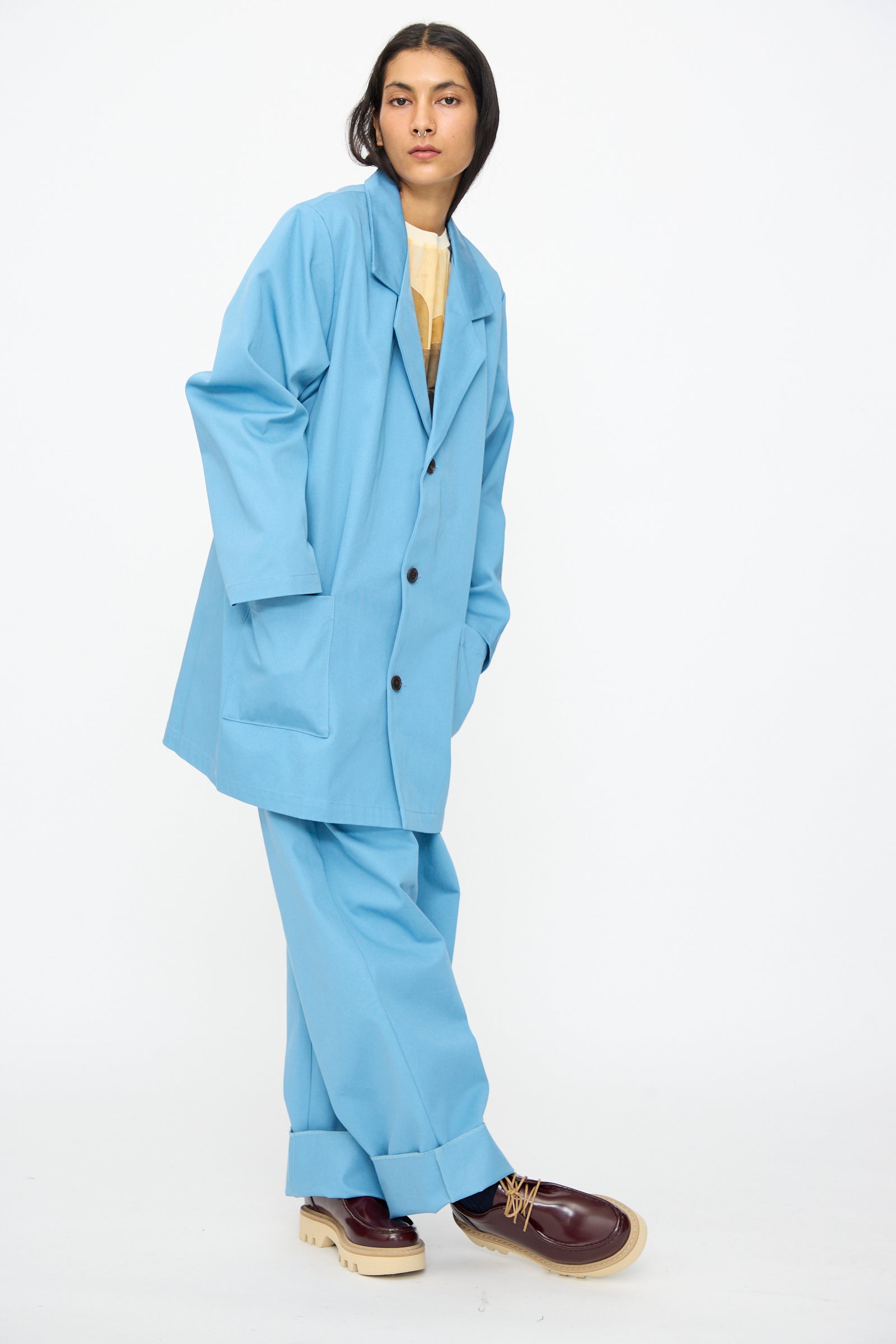 A model wears the Bless No. 81 Summer Workcoat Short in Skyblue, styled with wide-leg pants and brown platform shoes, showcasing an oversized fit against a plain white background.