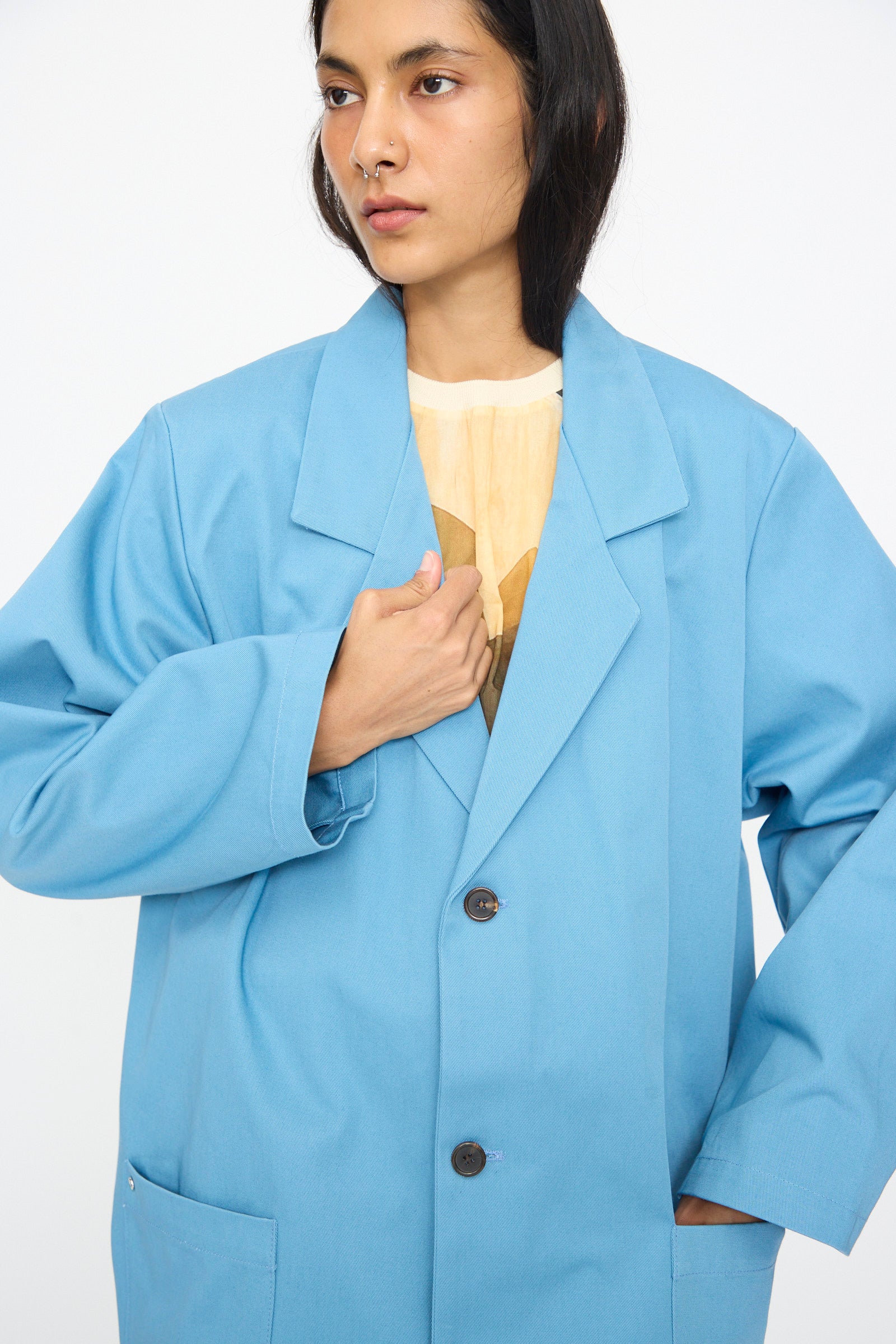 A person wearing the Bless No. 81 Summer Workcoat Short in Skyblue over a light yellow top stands against a plain white background, looking slightly to the side.