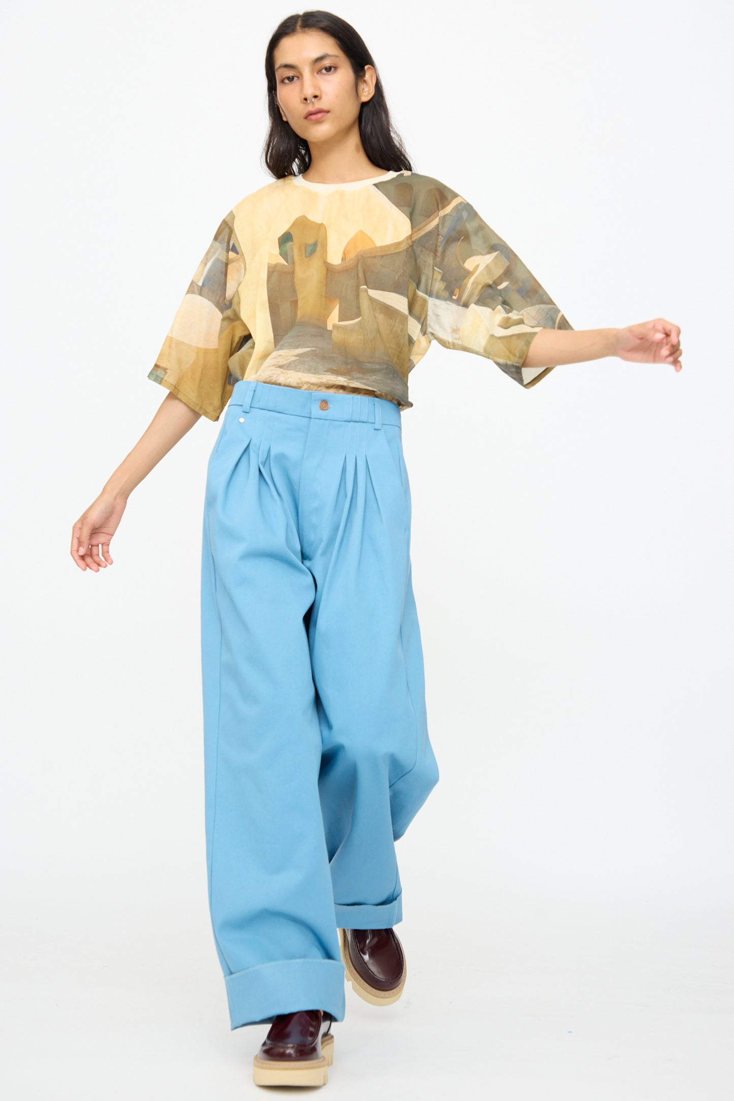 Model wears Bless No. 81 Ultrawidepleated Pant in Skyblue with a loose, abstract-patterned top and platform shoes, posing against a plain white background.