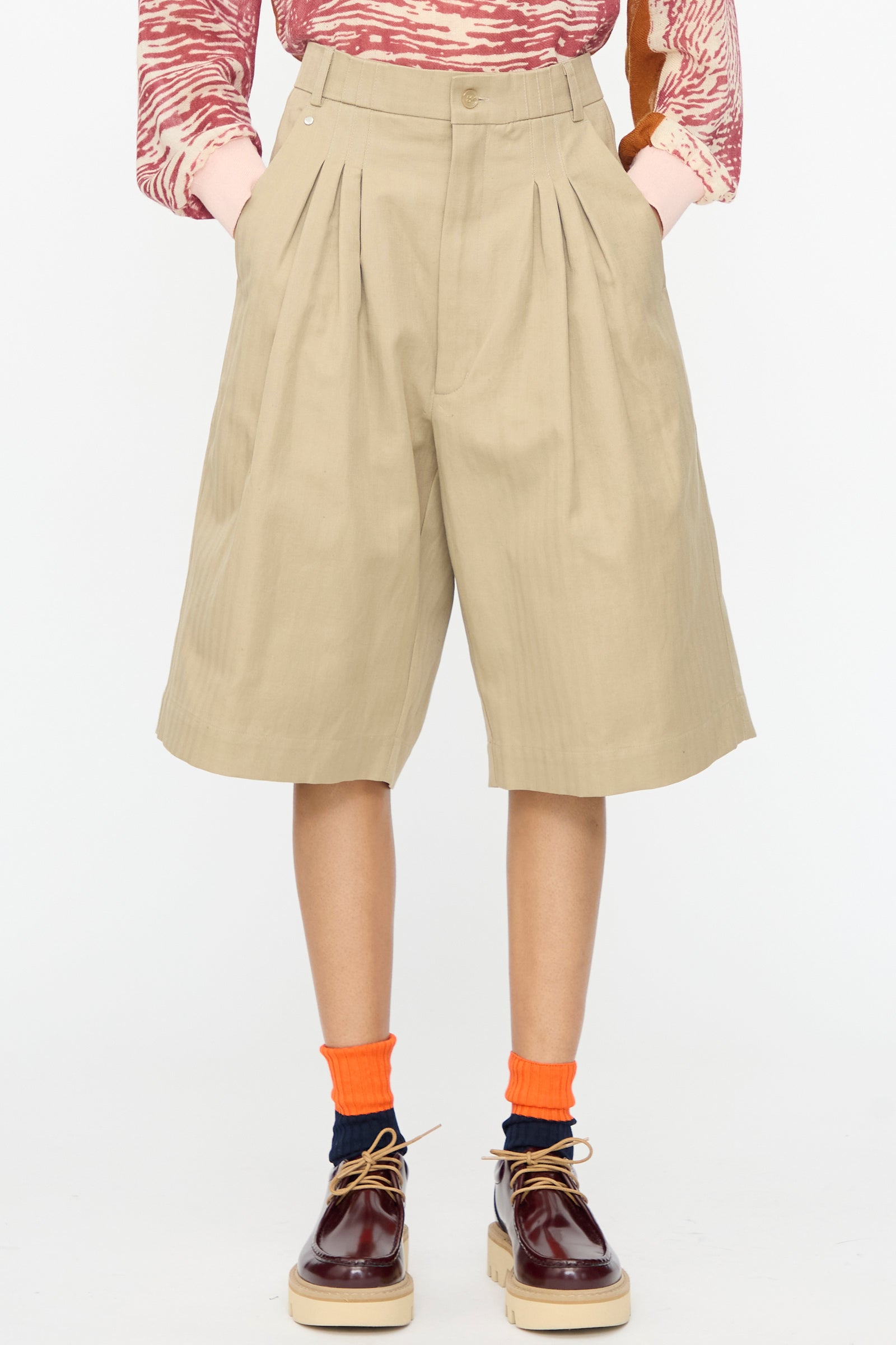 Wearing Bless No. 81 Ultrawidepleated Shorts in Sandkoeper, a red patterned long-sleeve shirt, orange and dark socks, and burgundy platform loafers. Hands are in pockets.