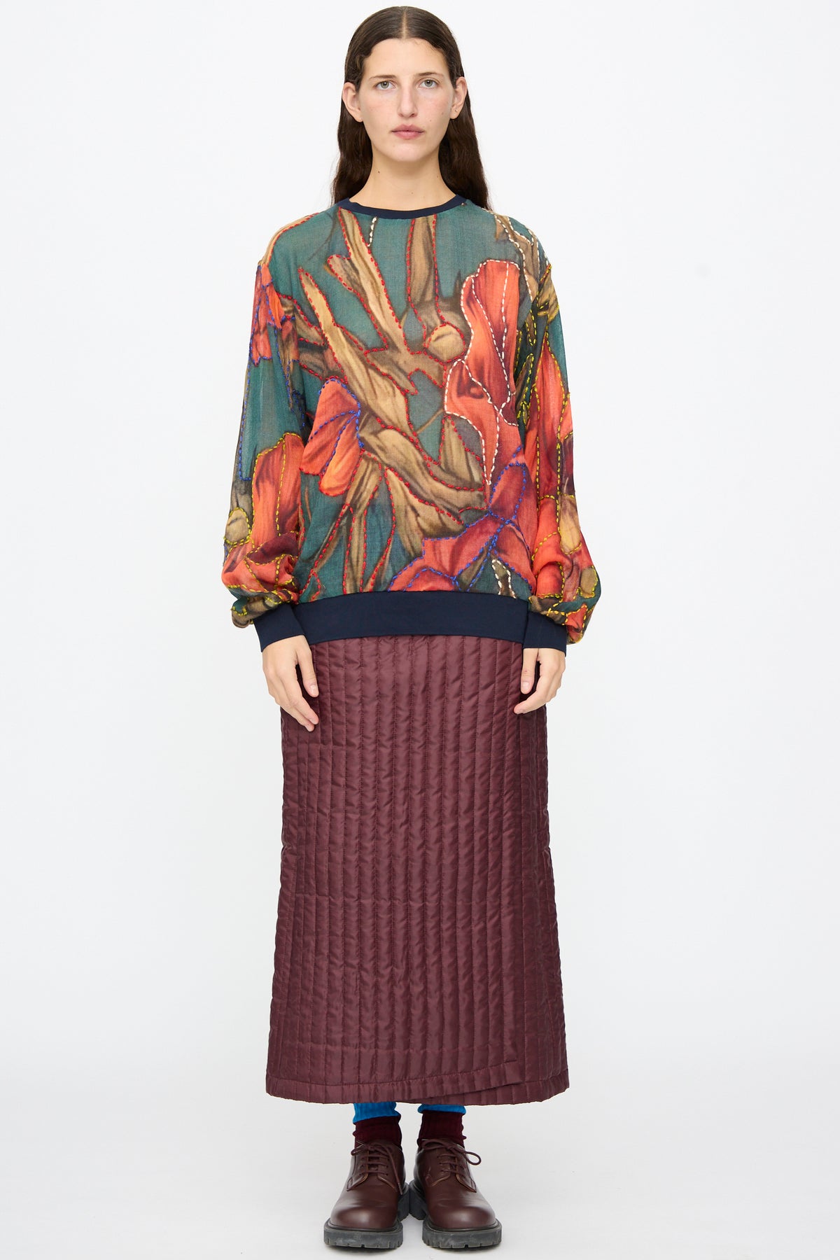 A person wears a Bless No. 82 Embroidered Sweater in Dark Brown and Green with a dark-brown quilted maxi skirt.