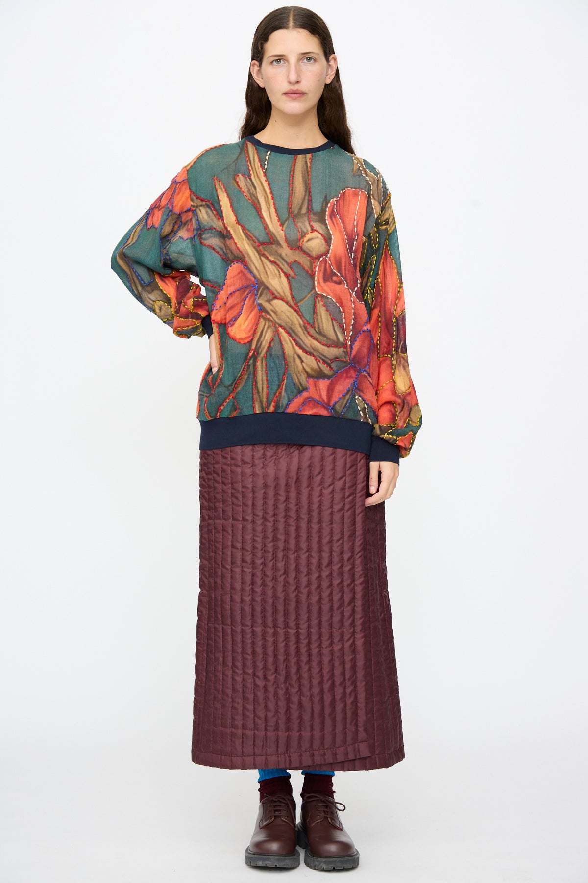 A person wearing a Bless No. 82 Embroidered Sweater in Dark Brown and Green and a dark-brown quilted maxi skirt.