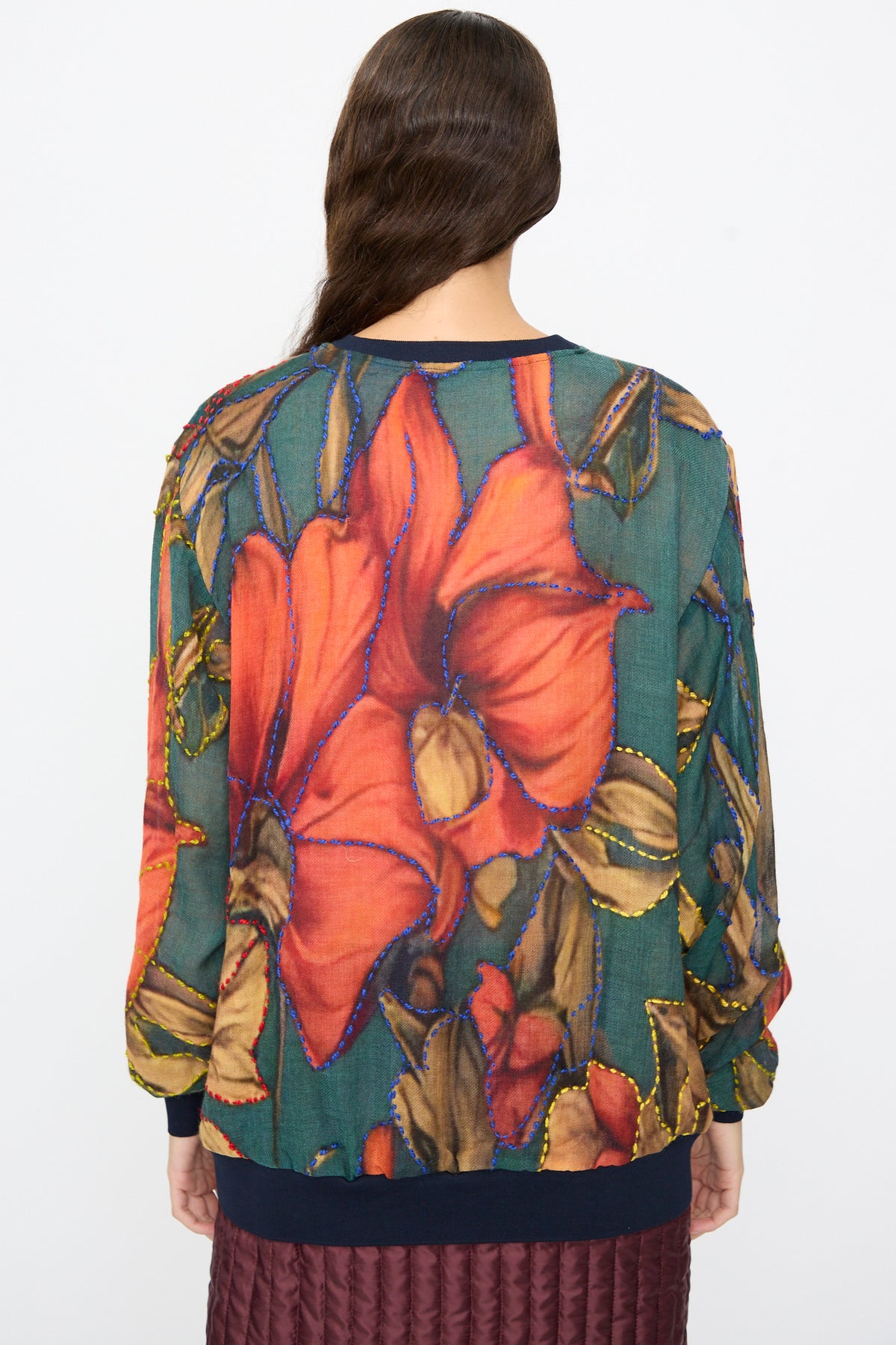 Back view of a person wearing a dark brown and green Bless No. 82 Embroidered Sweater, decorated with a large pattern outlined in colorful stitching.