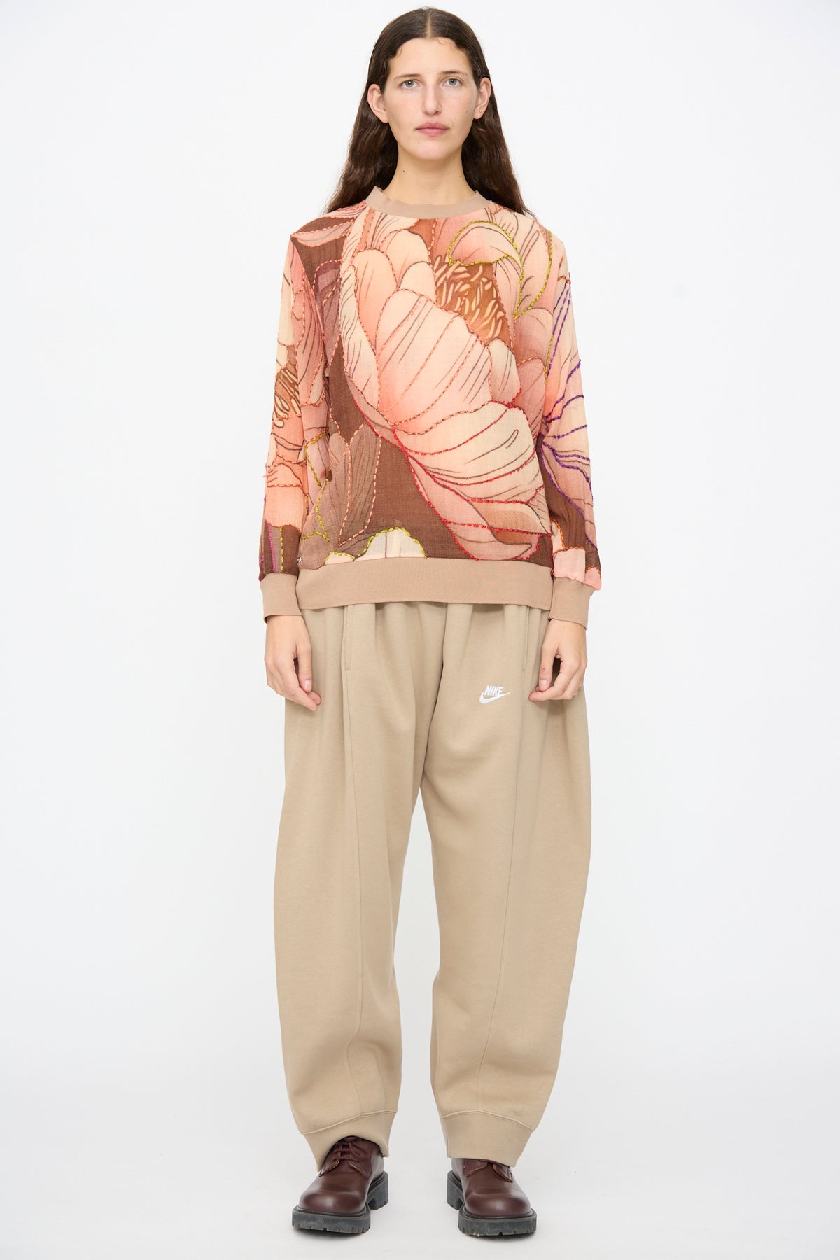 A person wears a Bless No. 82 Embroidered Sweater in Multicolor Beige and Rosé, paired with tan sweatpants and dark brown shoes.