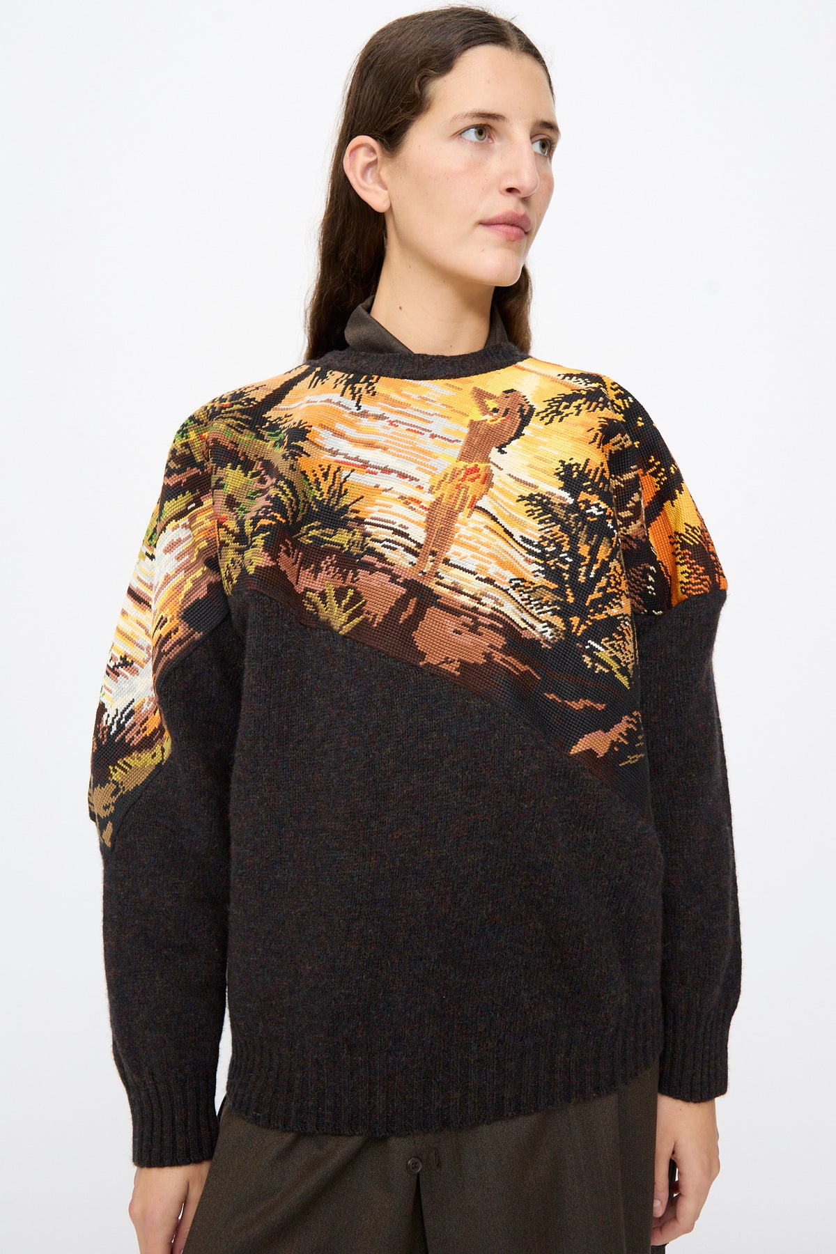 Person wearing a Bless No. 82 Kitschenrich in Unique Ultralarge Patchwork II wool pullover sweater with a brown base and a graphic landscape needlepoint motif across the chest and shoulders.