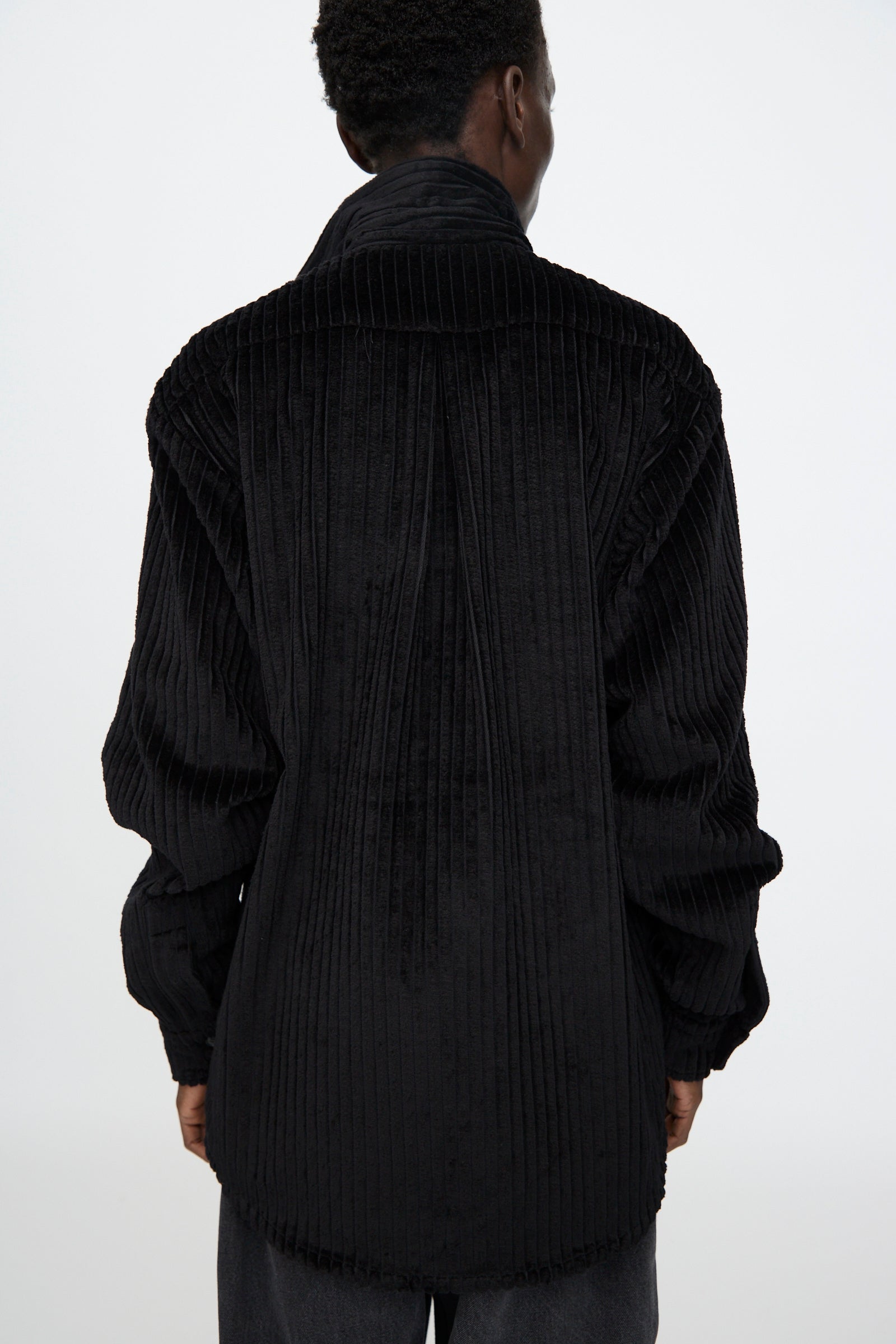 A person is shown from the back wearing the Bless No. 68 Neckerchiefer, a loose-fitting, asymmetrical long sleeve shirt in black corduroy, against a plain white background.