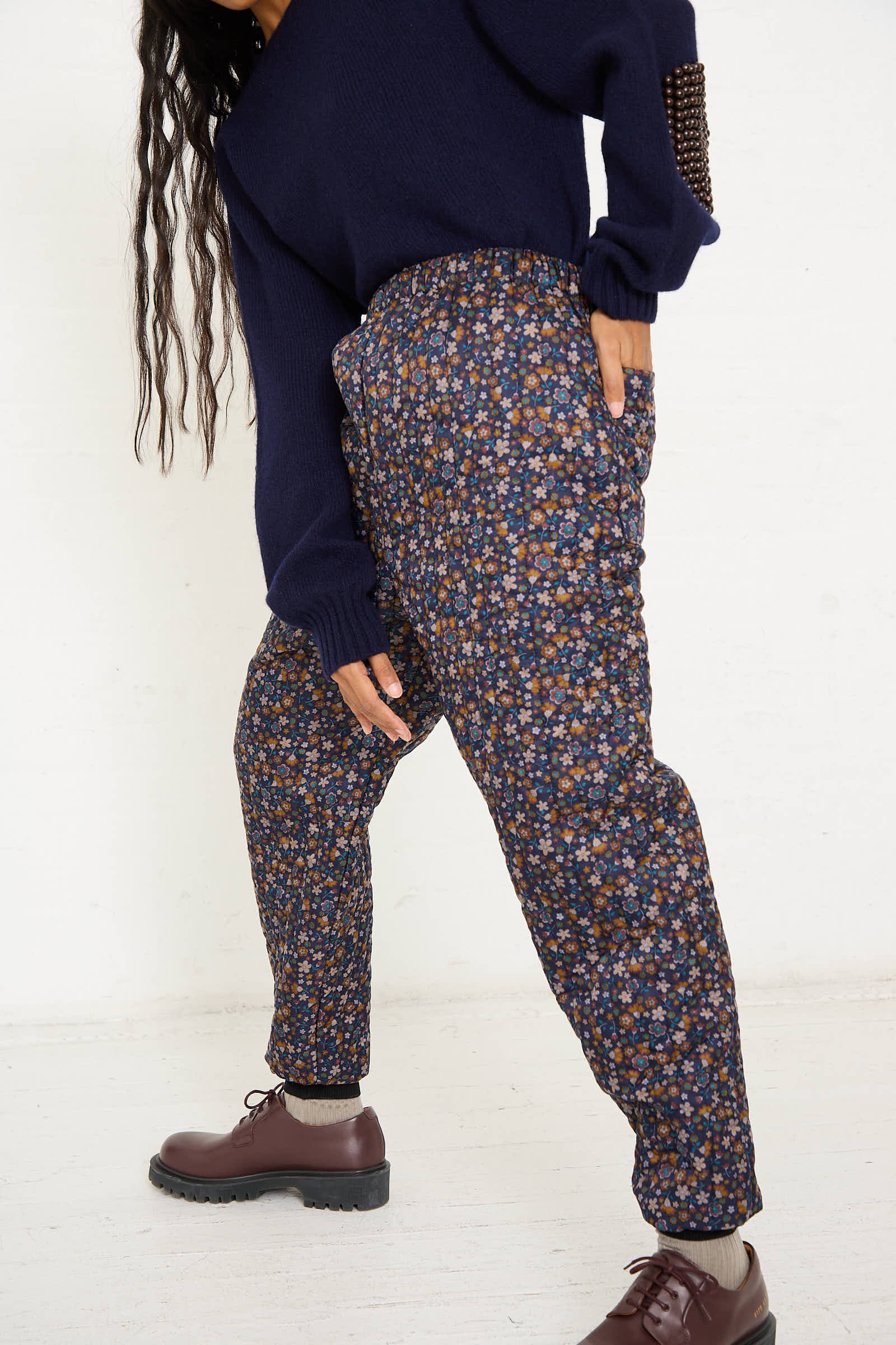 Person wearing a navy sweater and the No. 08 Monpe Pant in Navy Floral Multi by Bless, posing with hands in pockets against a plain white background.