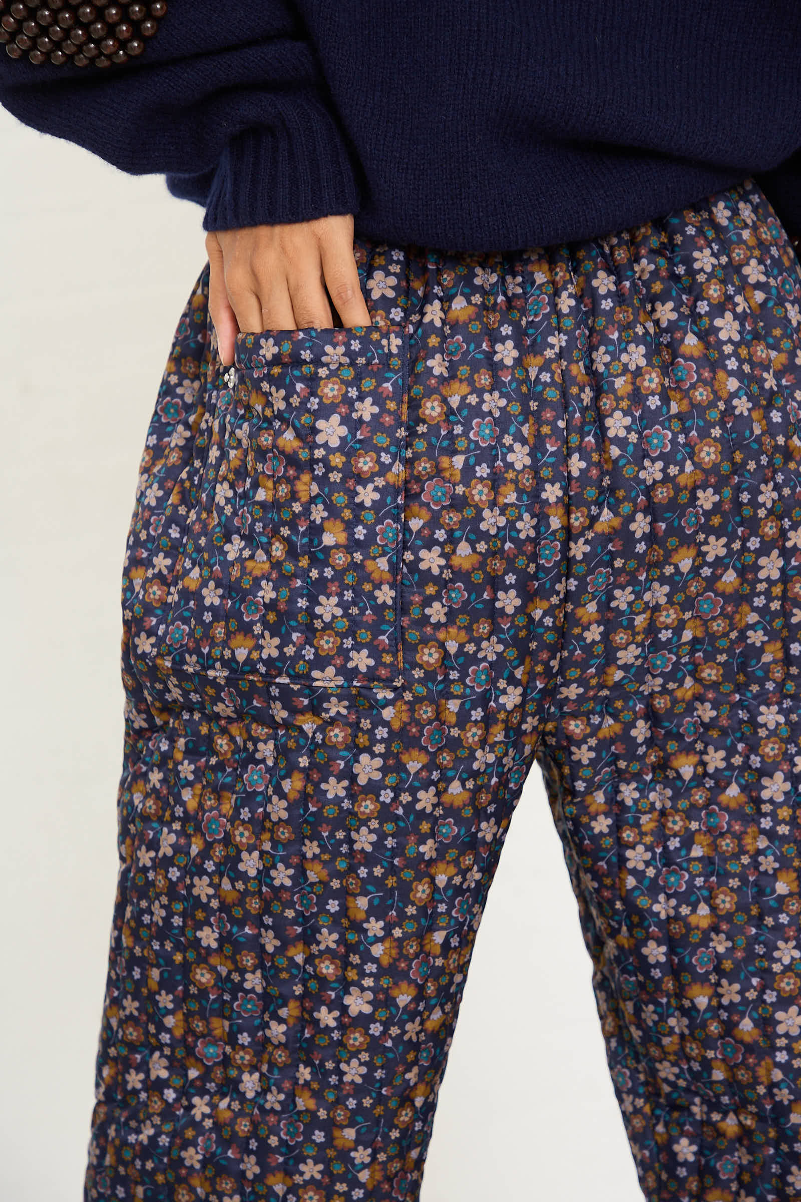 Close-up of a person wearing the No. 08 Monpe Pant in Navy Floral Multi by Bless, featuring a relaxed fit and a hand placed in a pocket. The person is also wearing a dark blue top.