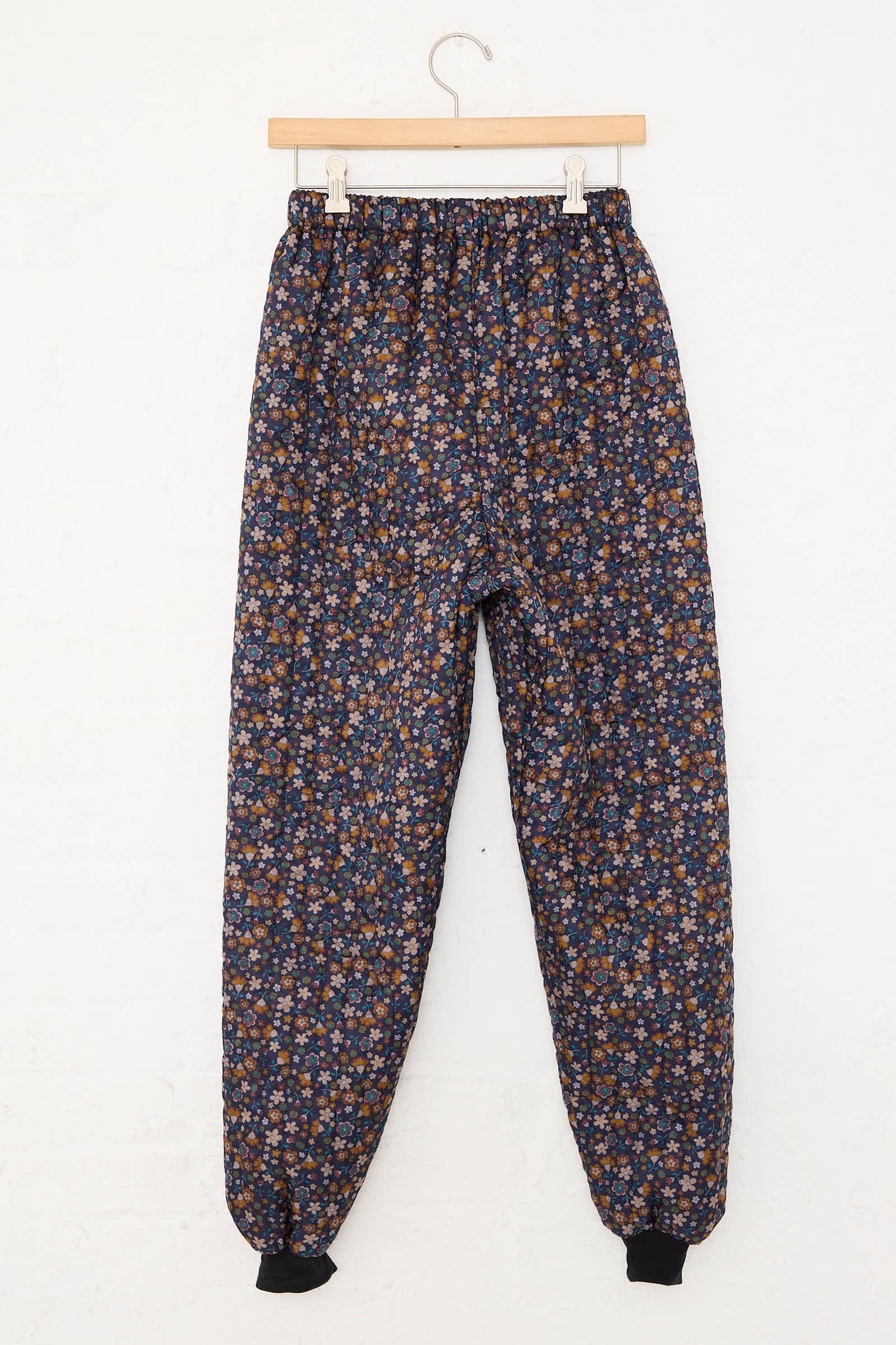 Hanging pair of No. 08 Monpe Pants in Navy Floral Multi by Bless, featuring blue, orange, and white flowers, with an elastic waistband and cuffs. 