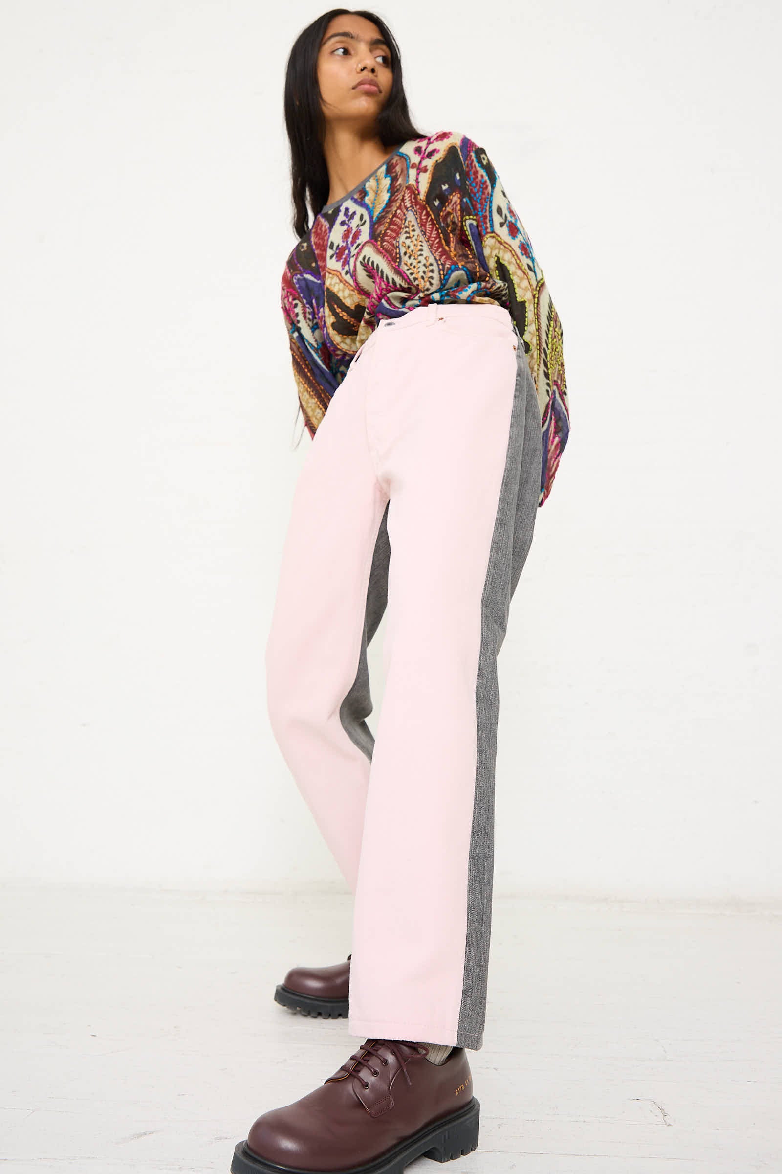 Woman wearing a colorful long-sleeve shirt, relaxed fit No. 73 Jeanspleatfront in Pink/Black by Bless, and brown boots, standing against a plain white background.