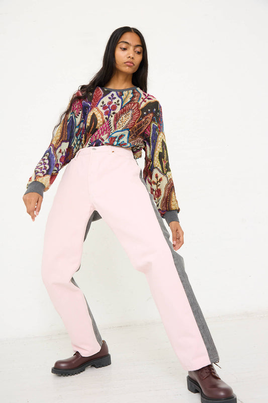 A person in a colorful patterned shirt and No. 73 Jeanspleatfront in Pink/Black by Bless poses with legs apart against a plain background, wearing dark brown shoes.