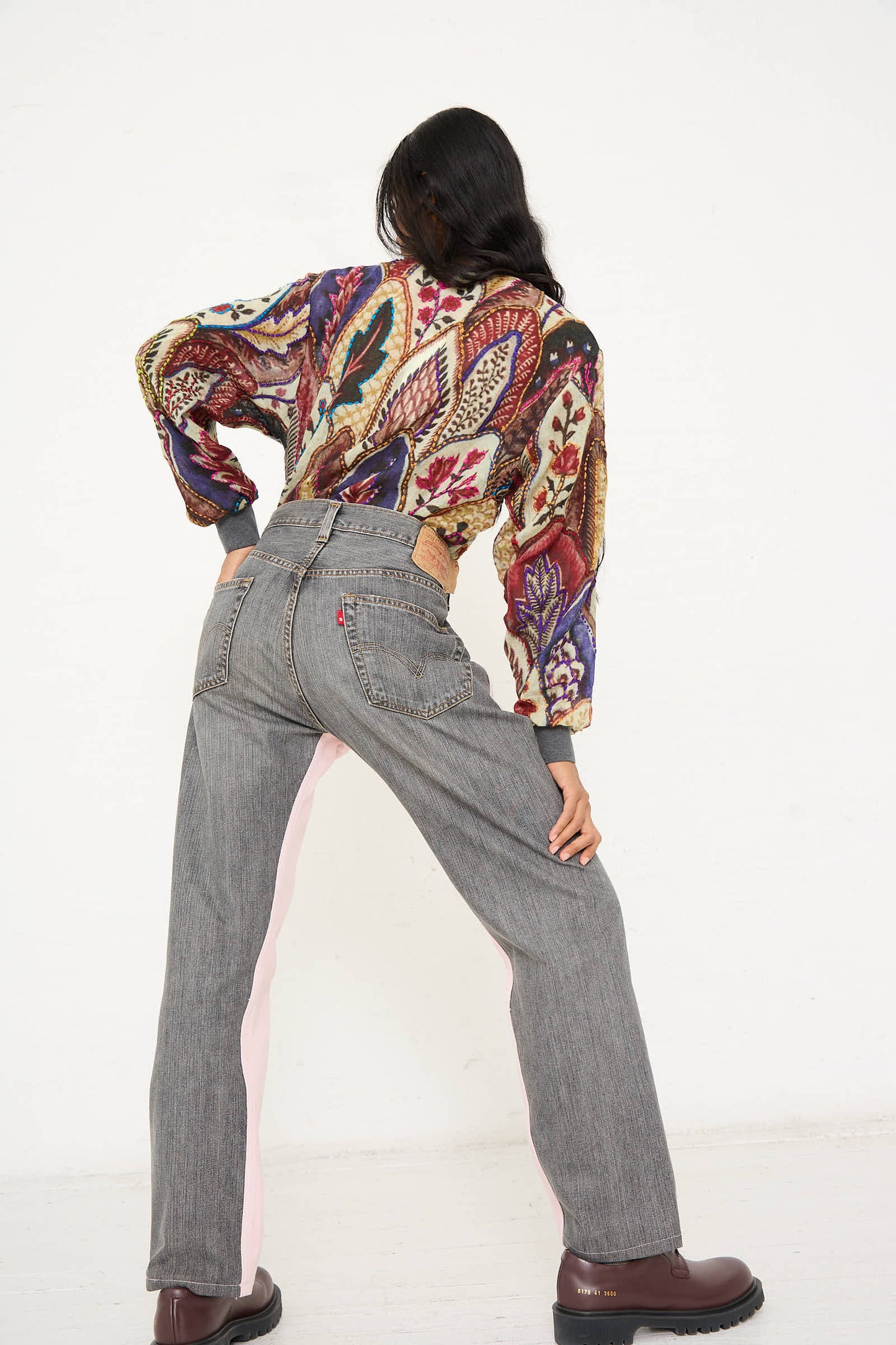 A person wearing a colorful, patterned blouse and the Bless No. 73 Jeanspleatfront in Pink/Black poses with their back to the camera.