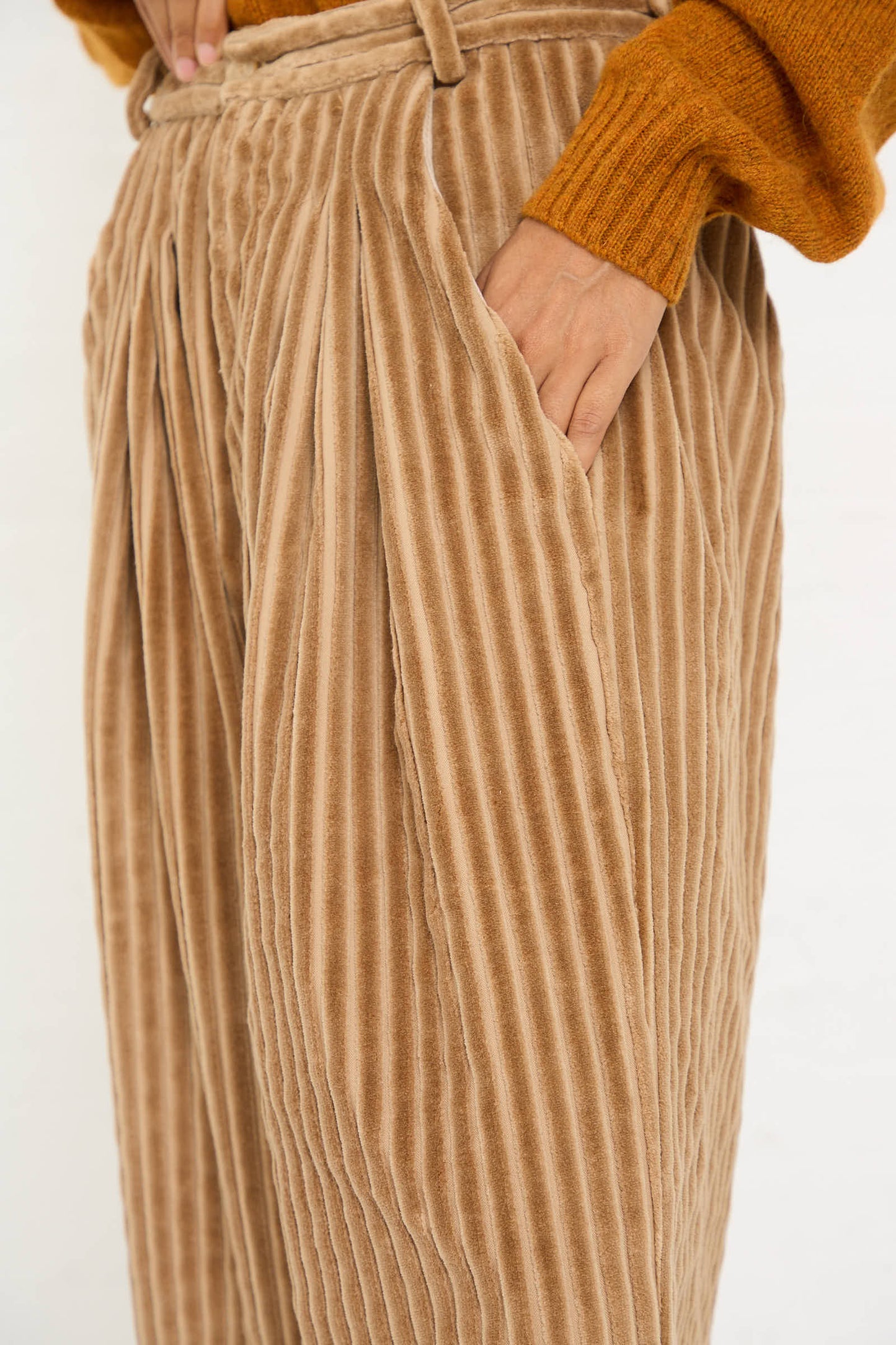 Person wearing the No. 78 Ultrawidepleated Pant in Jumbo Beige Cord by Bless and an orange sweater, with one hand in their pocket.