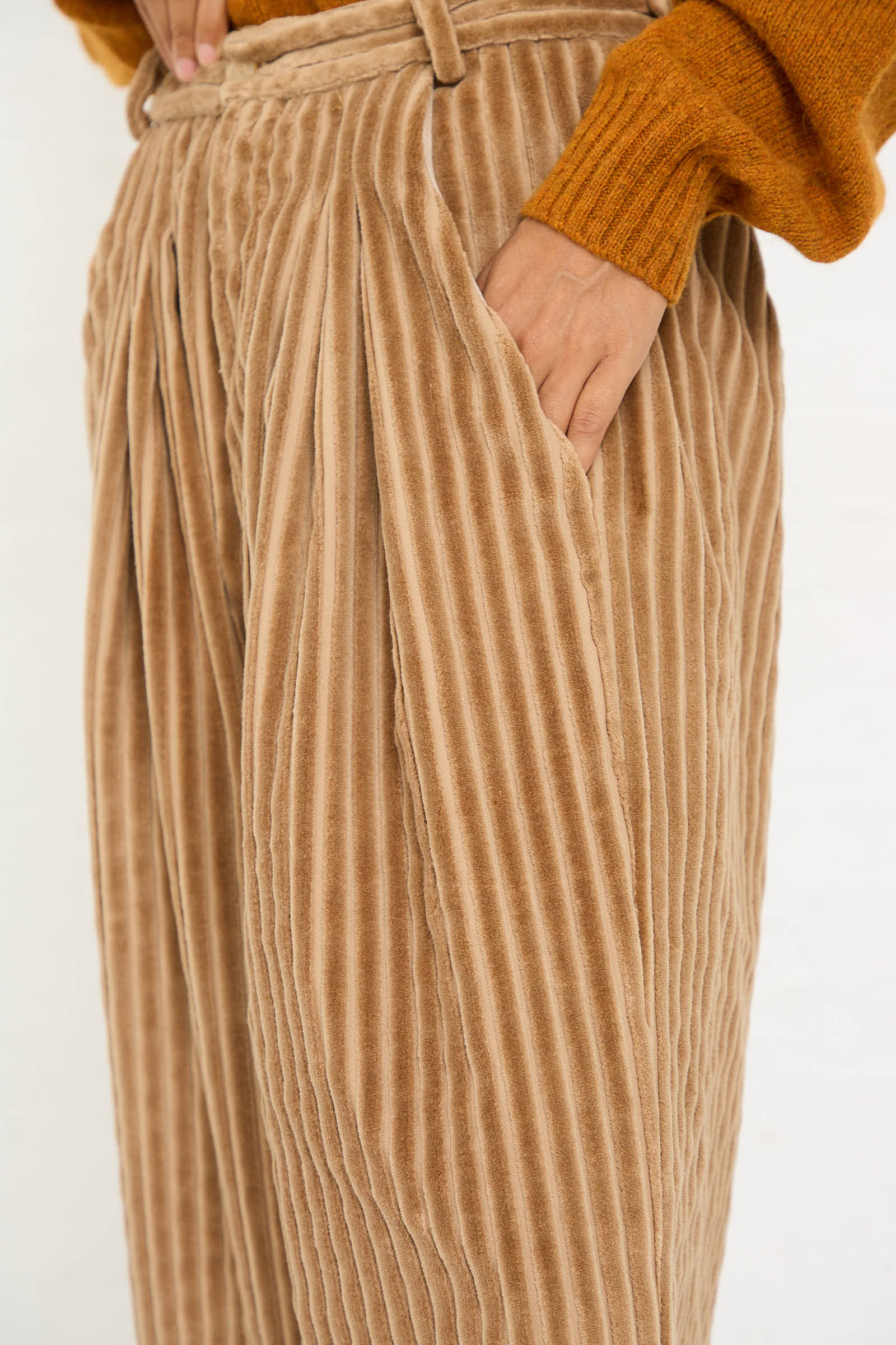 Person wearing the No. 78 Ultrawidepleated Pant in Jumbo Beige Cord by Bless and an orange sweater, with one hand in their pocket.