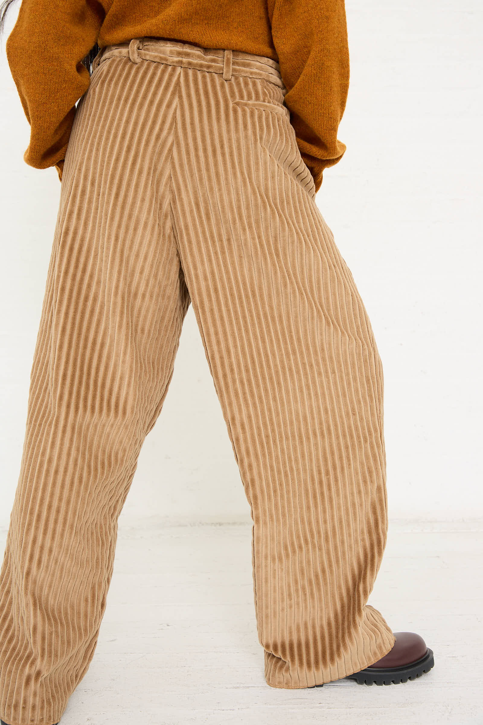 A person wearing a rust-colored sweater effortlessly pairs it with the relaxed-fit Bless No. 78 Ultrawidepleated Pant in Jumbo Beige Cord, standing against a plain background.