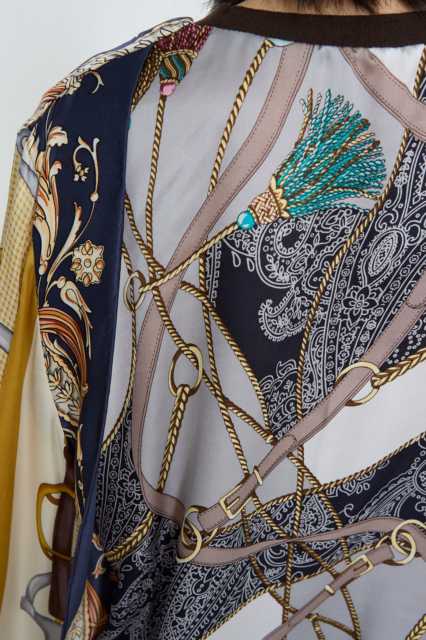 A close-up of the Windy Silkscarves Top by Bless features a detailed vintage scarf design, showcasing ropes, chains, and paisley patterns in vibrant teal, gold, and black. 