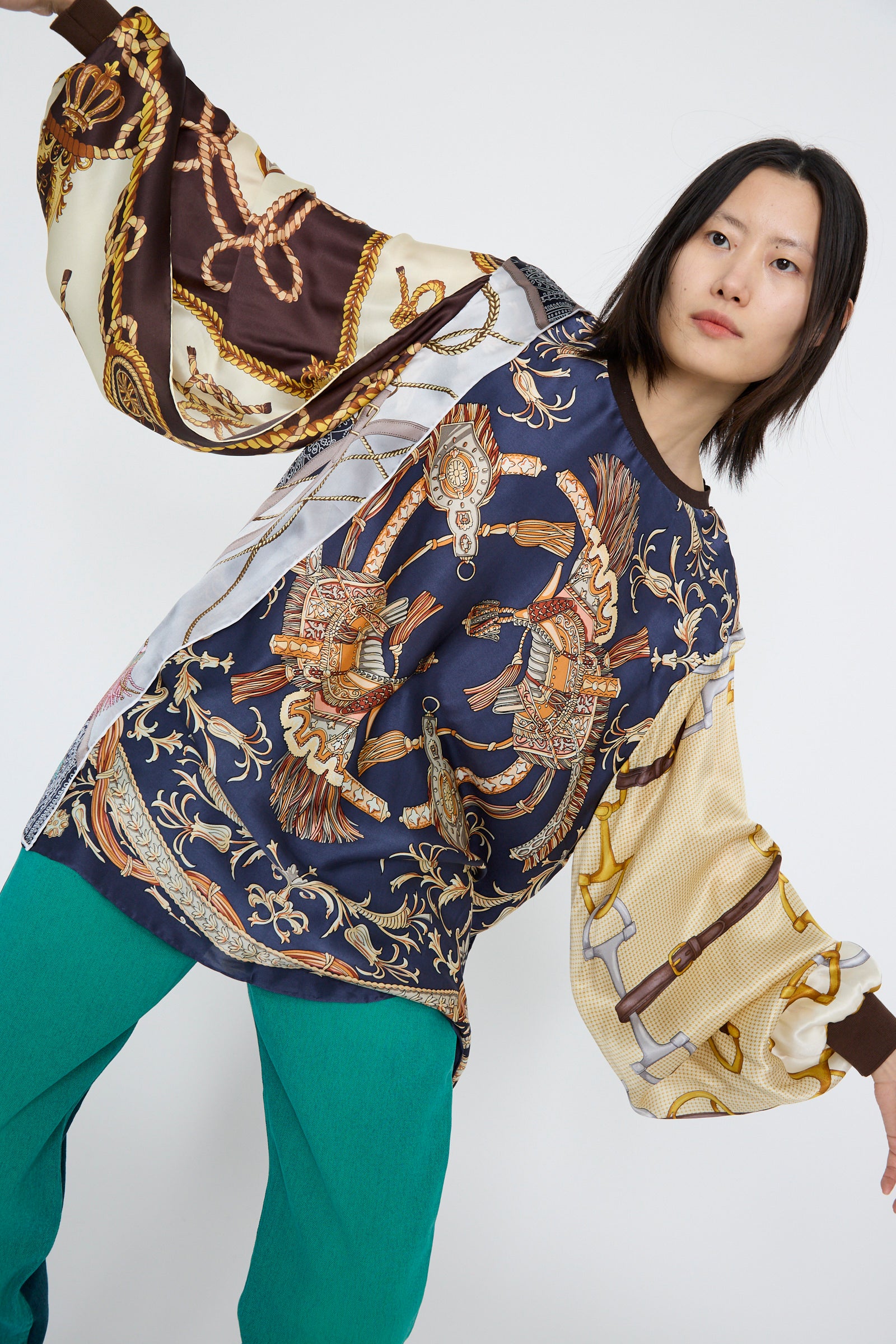 A model styled in the Bless Windy Silkscarves Top with green, brown, and yellow prints poses against a plain background, paired with green pants and vintage scarves.