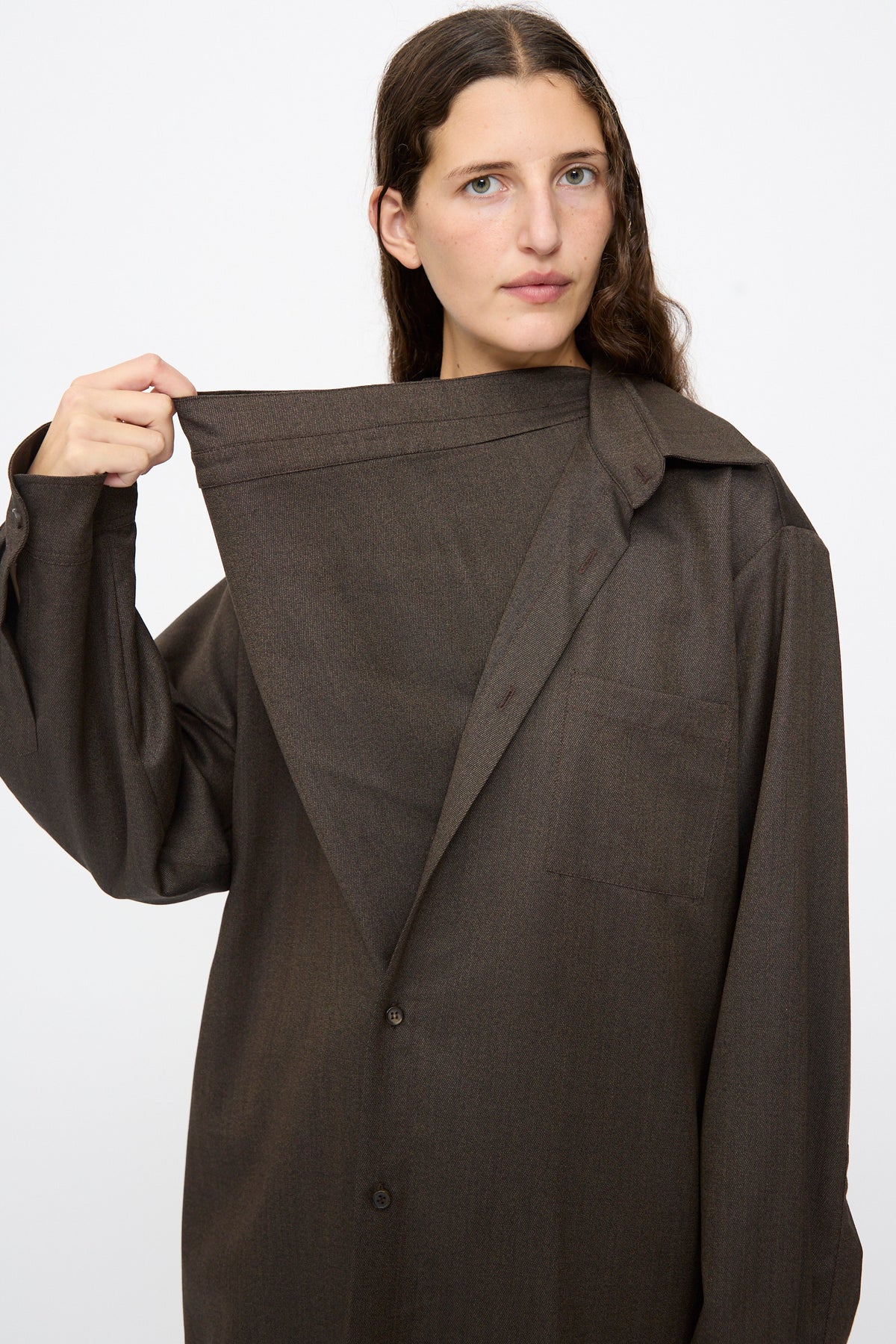 A person wearing the brown melange Wool No. 82 Neckerchiefdress lifts the oversized, asymmetrical scarf collar to reveal the chest area.