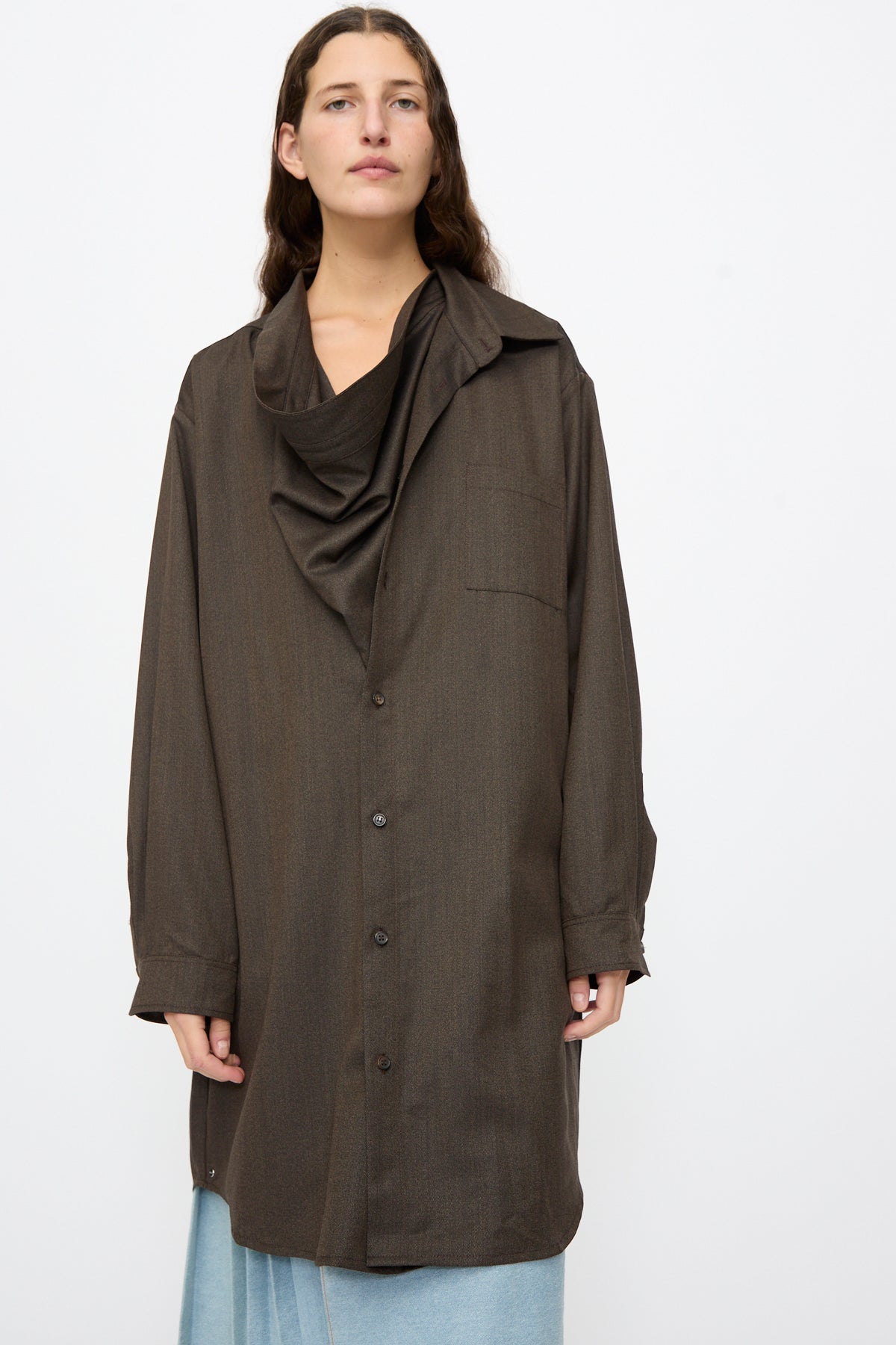 A person wearing a Bless Wool No. 82 Neckerchiefdress in brown melange, featuring an oversized fit, asymmetrical scarf collar, and a draped, cowl-style neckline.