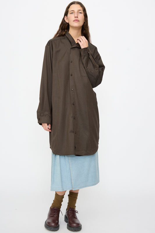 A person wearing a Bless Wool No. 82 Neckerchiefdress in Brown Melange over a light blue wrap skirt, brown socks, and dark oxfords.