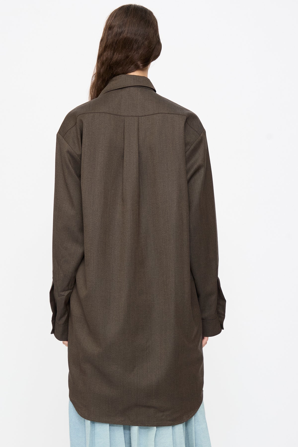 Back view of a person wearing a brown melange Wool No. 82 Neckerchiefdress by Bless with an asymmetrical scarf collar over a light blue skirt.