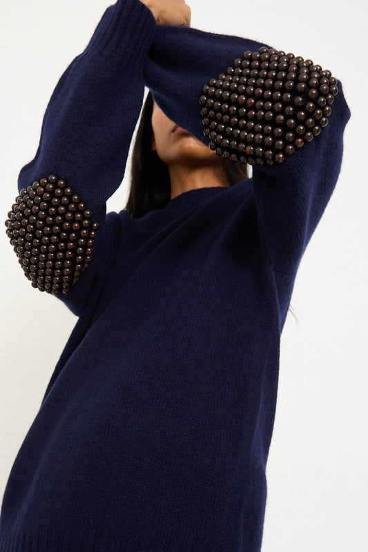 Person wearing the Bless Wool No. 75 Pearlpad Sweater in Navy with Wooden Pearls, covering their face with their sleeve.