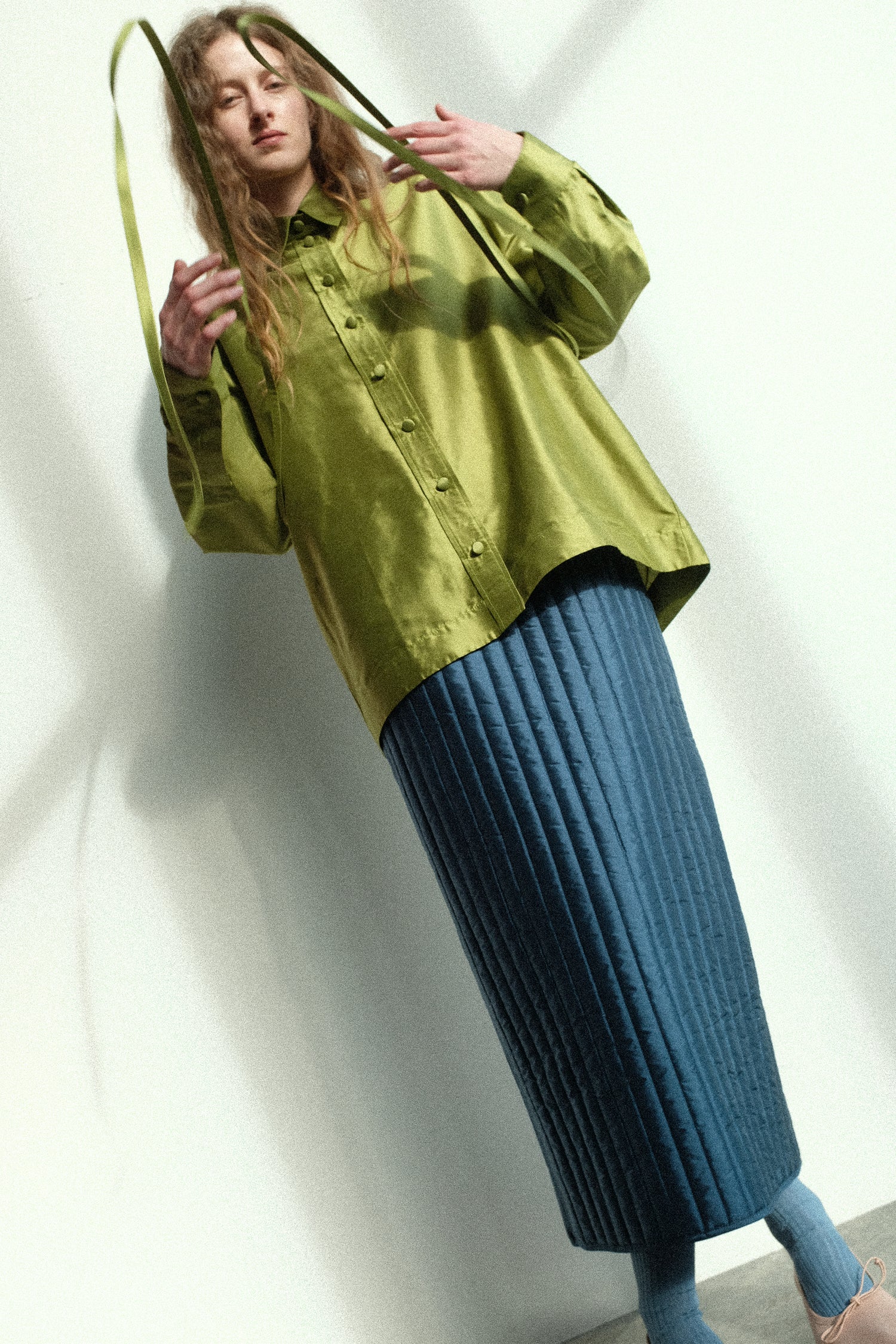 A woman wearing Cawley's Silk Dupion June Shirt in Apple, Quilted Silk Sadie Skirt in Insignia against a white wall.
