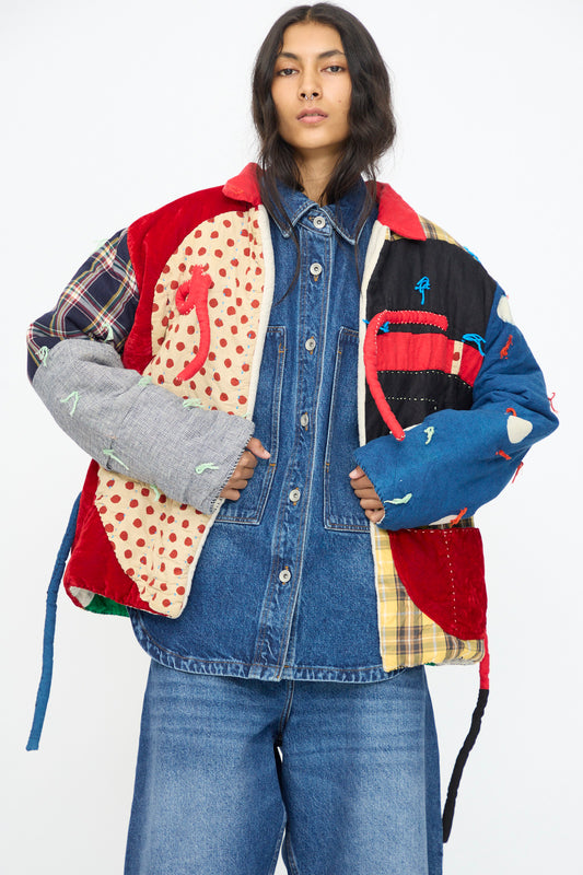 A person wears the CMC Polka Assembly Coat, a hand-quilted 100% cotton piece made in New York, over an oversized denim shirt and wide-leg jeans, standing against a plain white background.