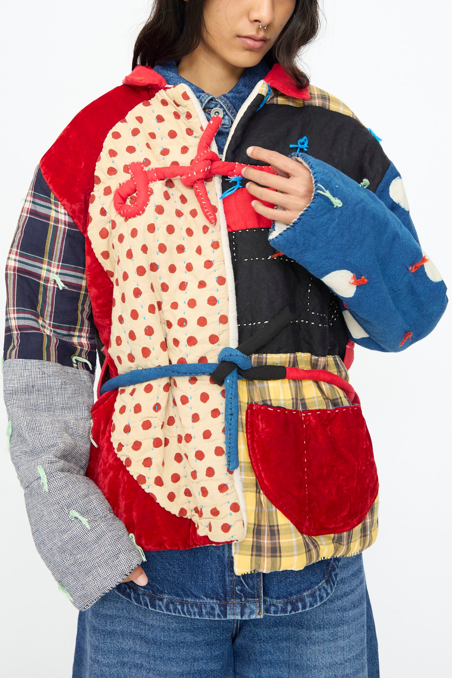 A person wears the Polka Assembly Coat by CMC—a colorful, hand-quilted 100% cotton coat made in New York with polka dot, plaid, and solid patterns. It ties at the waist with a blue string and is styled over denim.
