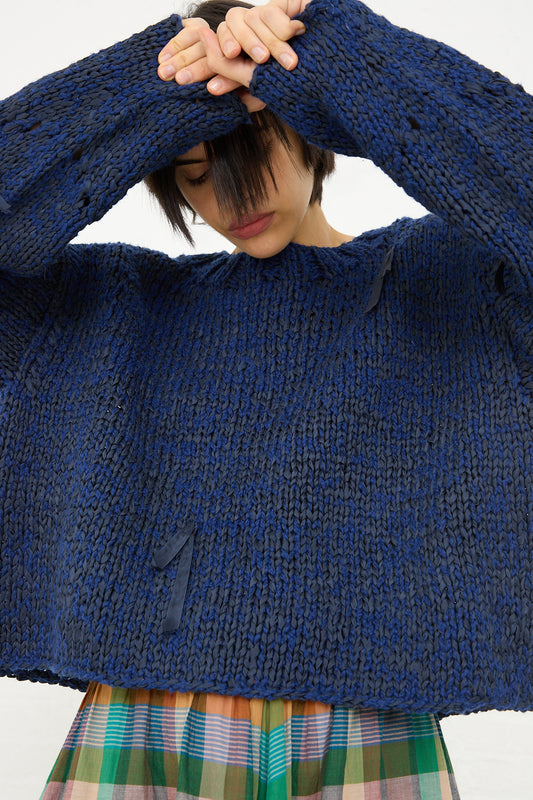 Woman in a Caron Callahan Boucle Cotton Yarn Hampton Sweater in Indigo with her hand on her forehead, partial view showing from nose up, against a white background.