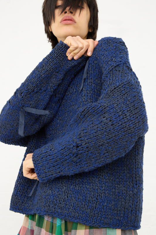 A person wearing a Caron Callahan Boucle Cotton Yarn Hampton Sweater in Indigo and a plaid skirt, with a focus on the clothing rather than the face.