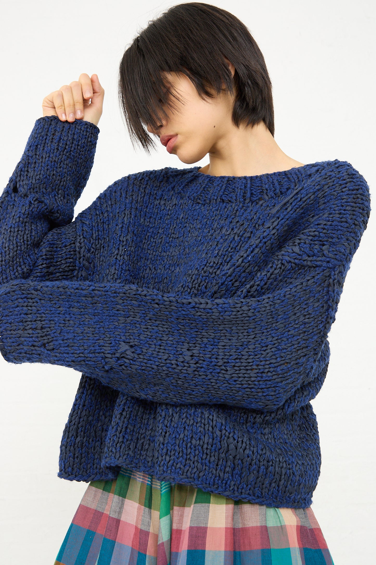 Woman in a blue, oversized Boucle Cotton Yarn Hampton sweater by Caron Callahan with her arm raised, looking downward.