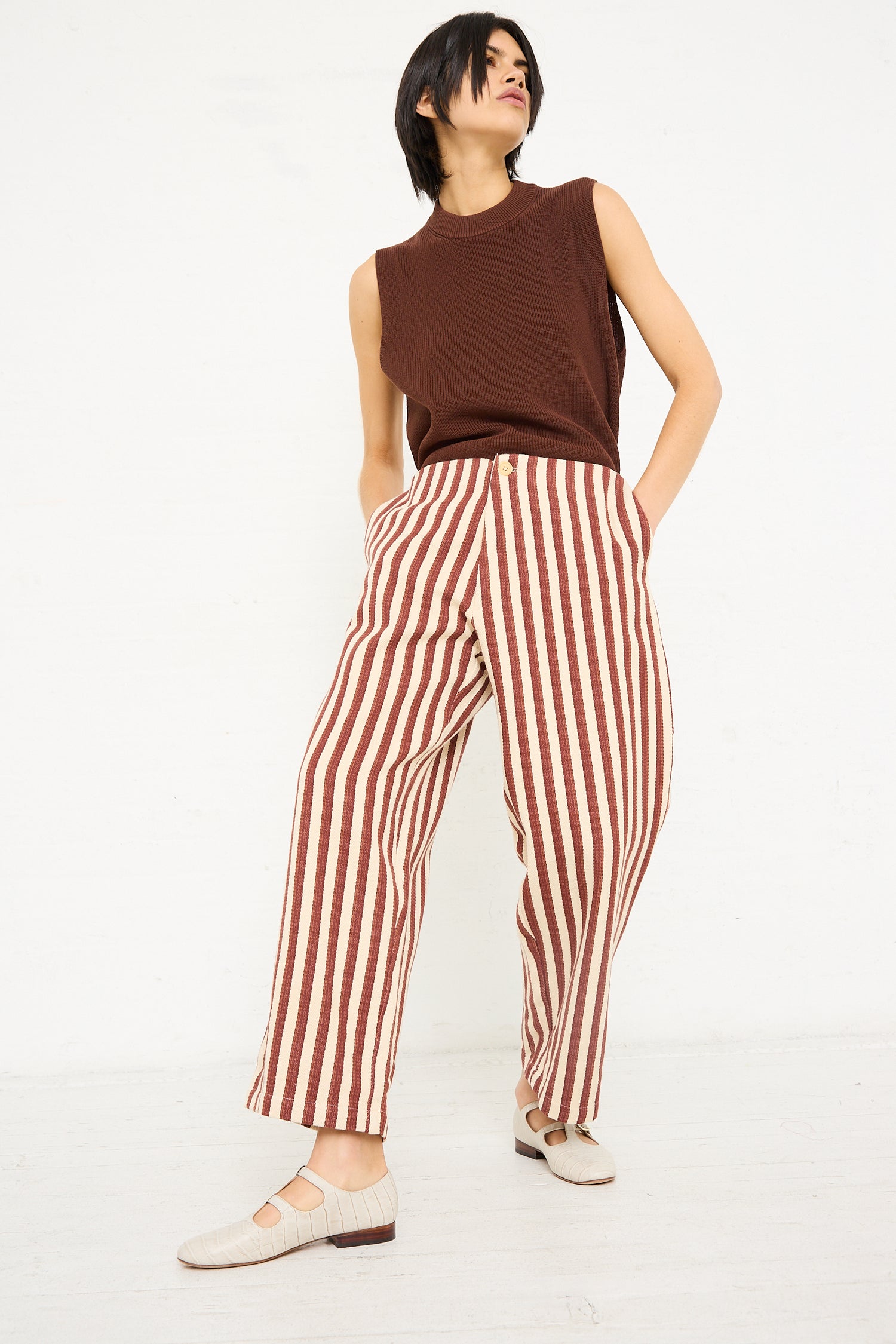 A woman stands in a casual pose wearing Caron Callahan's Dexter Pant in Auburn Stripe and sleeveless brown top, with her hand tucked into a pocket.