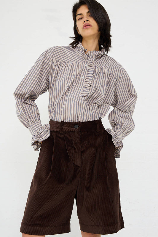 A person wearing a striped, long-sleeved blouse with a ruffled neckline and Cawley's British Cord Mara Short in Chocolate, featuring a relaxed fit. Everything is set against a plain white background.