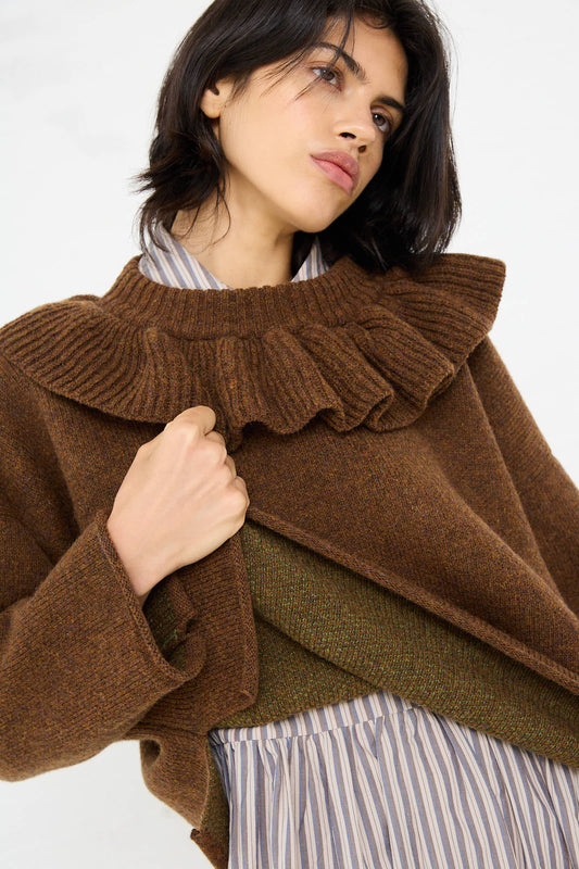 A woman wearing the Cawley British Lambswool Ruffle Jumper in Tobacco layered over a striped shirt gazes upward.