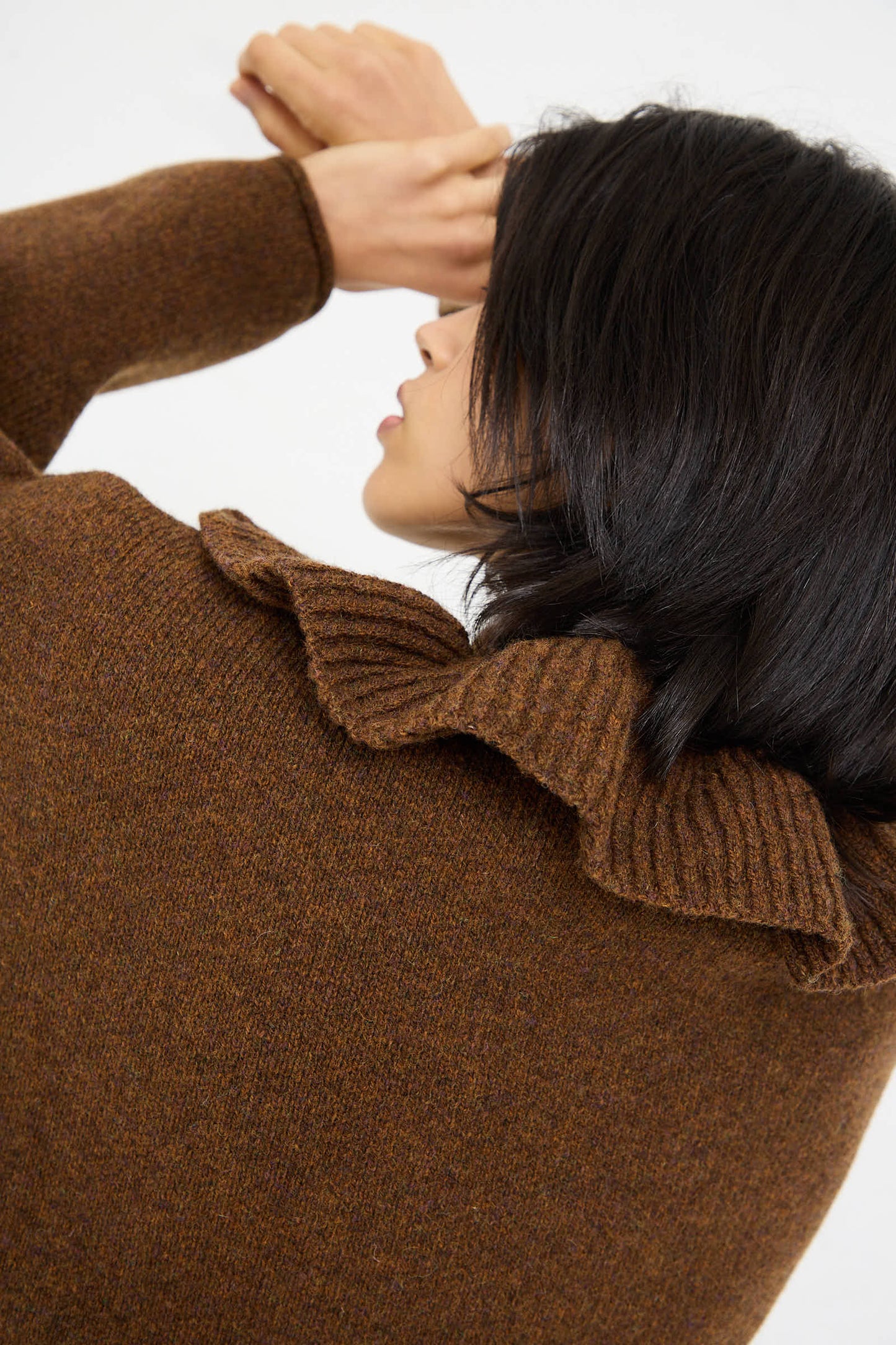 Person with medium-length dark hair, turned away, wearing the Cawley British Lambswool Ruffle Jumper in Tobacco.