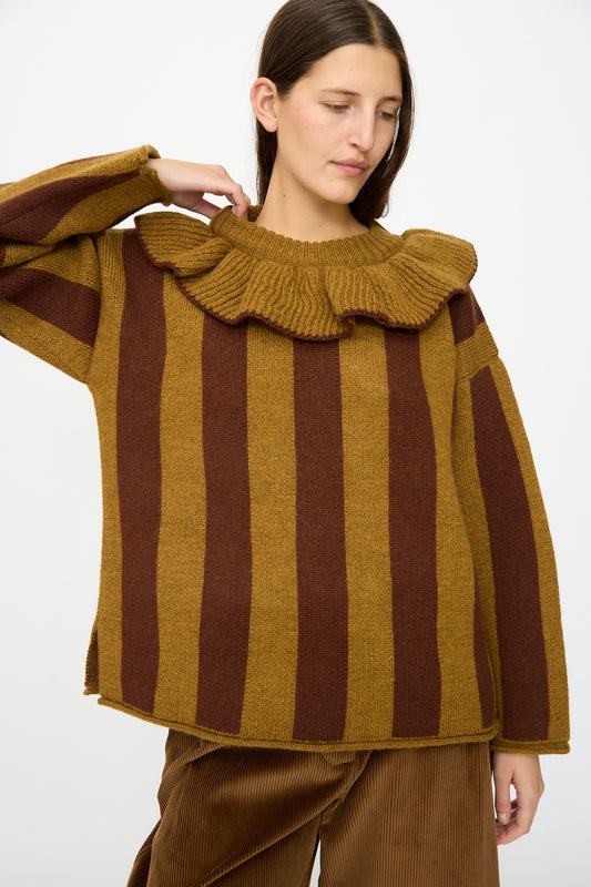 A person wearing the Cawley British Merino Wool Striped Ruffle Jumper in Goldfinch and Bordeaux, paired with brown corduroy pants, stands against a plain background.