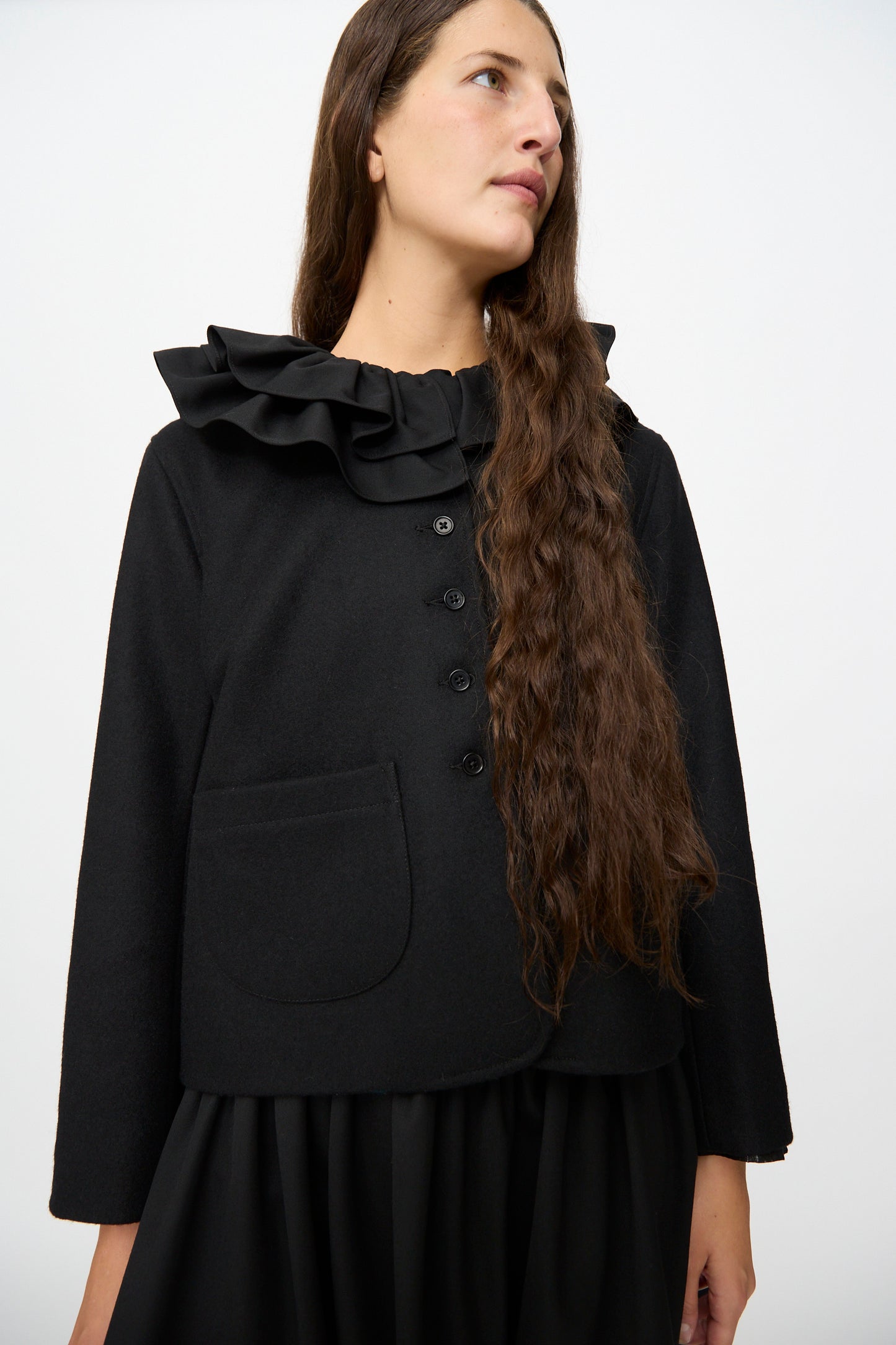 A woman wearing the Cawley British Wool Rowan Jacket in Black, featuring a ruffled collar, stands against a plain white background.