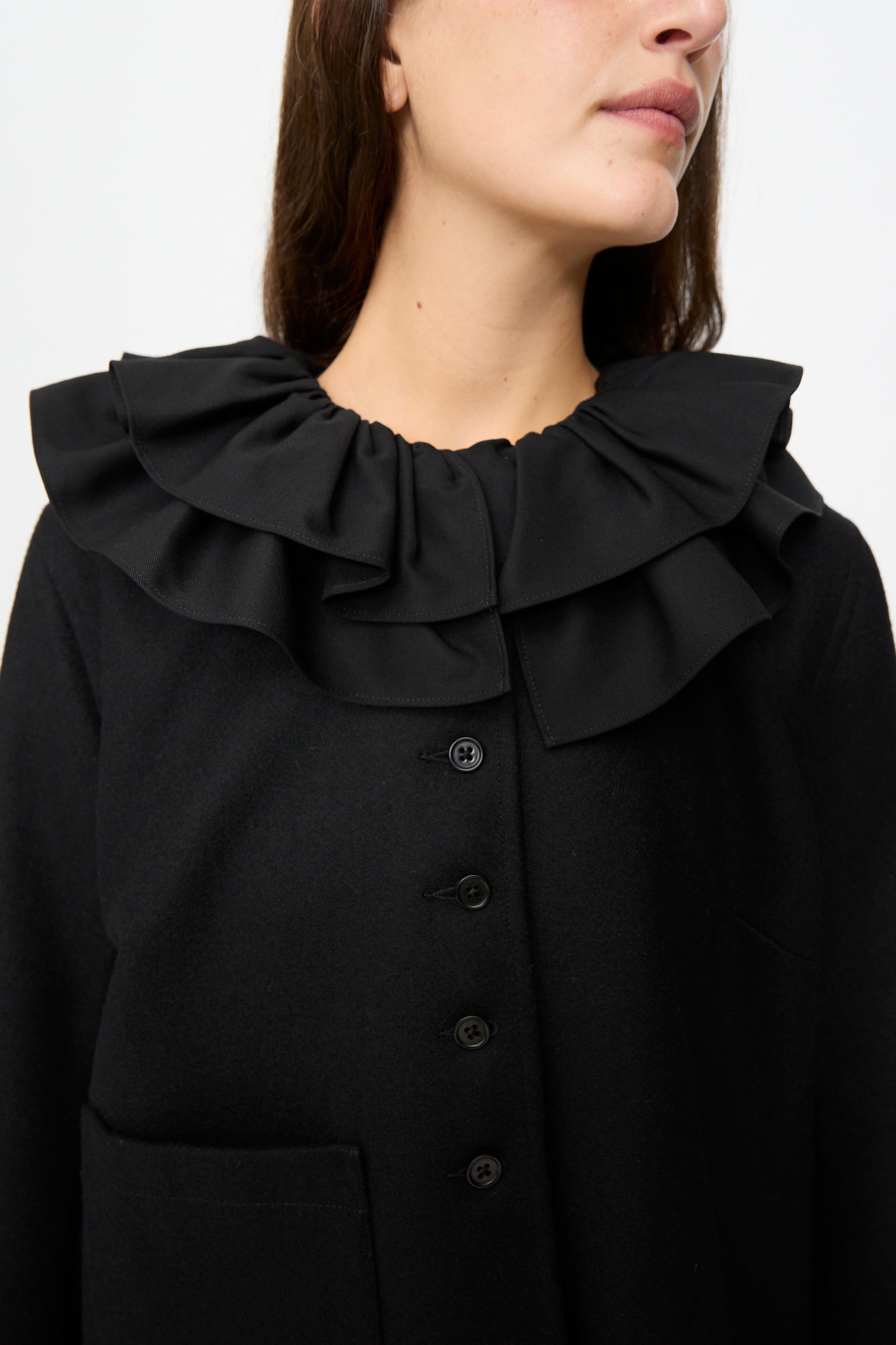 A woman models the Cawley British Wool Rowan Jacket in Black, featuring a large ruffled collar and button front. Shown from the shoulders to mid-chest against a plain background, this cropped jacket is crafted from British wool and merges classic elegance with contemporary style.
