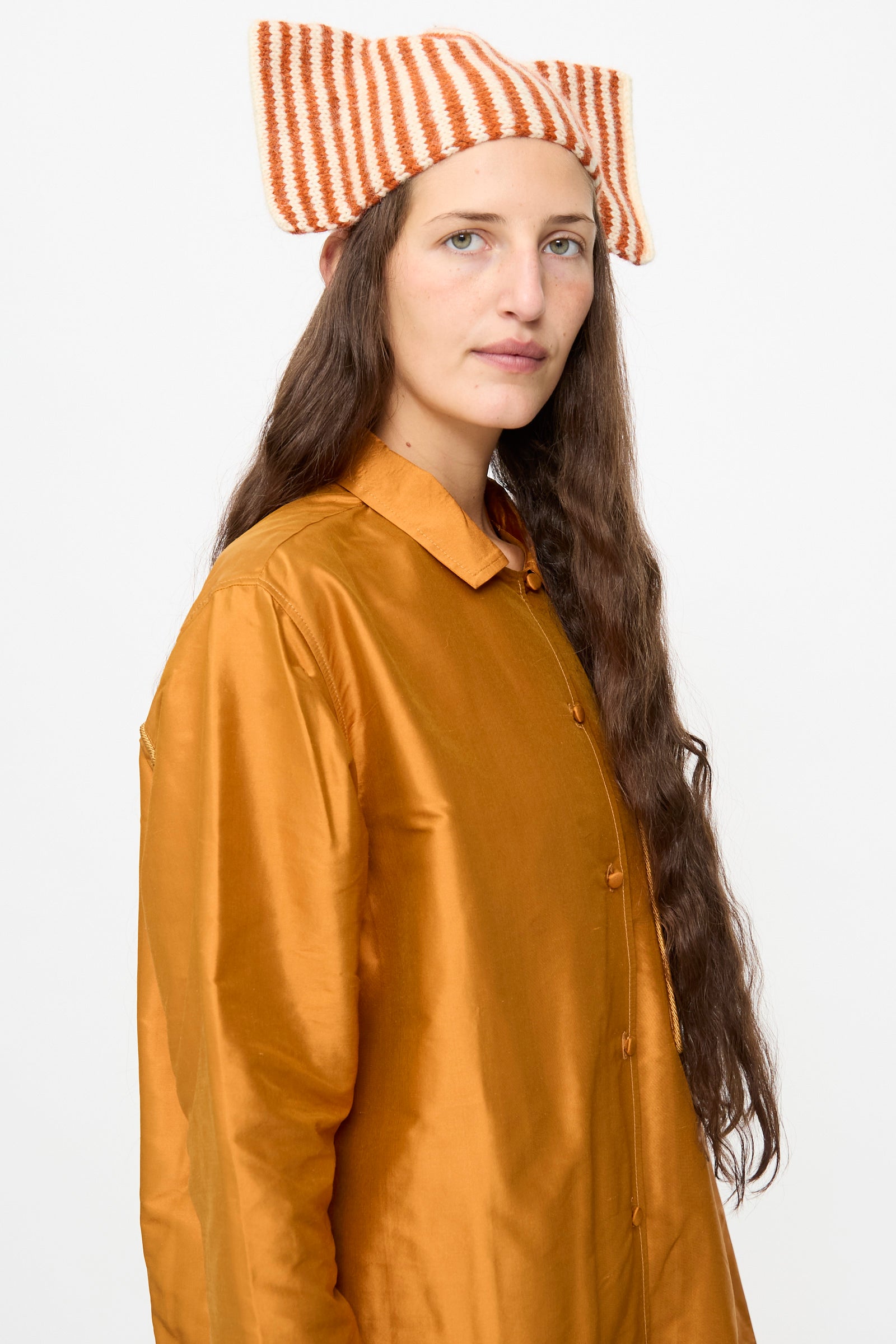 A person wearing a shiny orange button-up shirt and the Cawley Brushed British Wool Stripe Bow Hat in Natural and Autumn stands against a plain white background.
