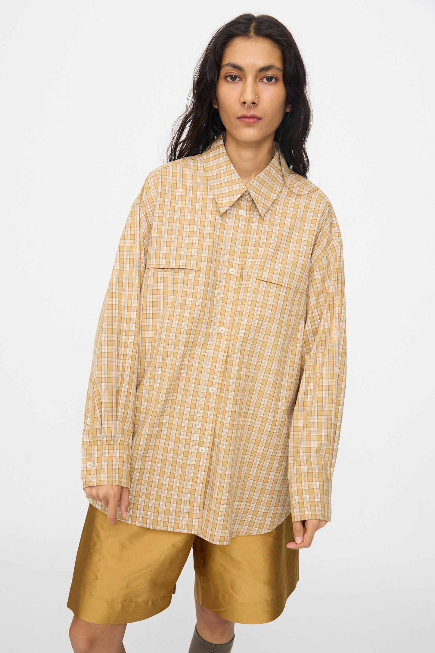 A person wearing the Cawley Checked Cotton Phoebe Shirt in Ochre, Red and Purple Check and tan shorts stands against a plain white background.