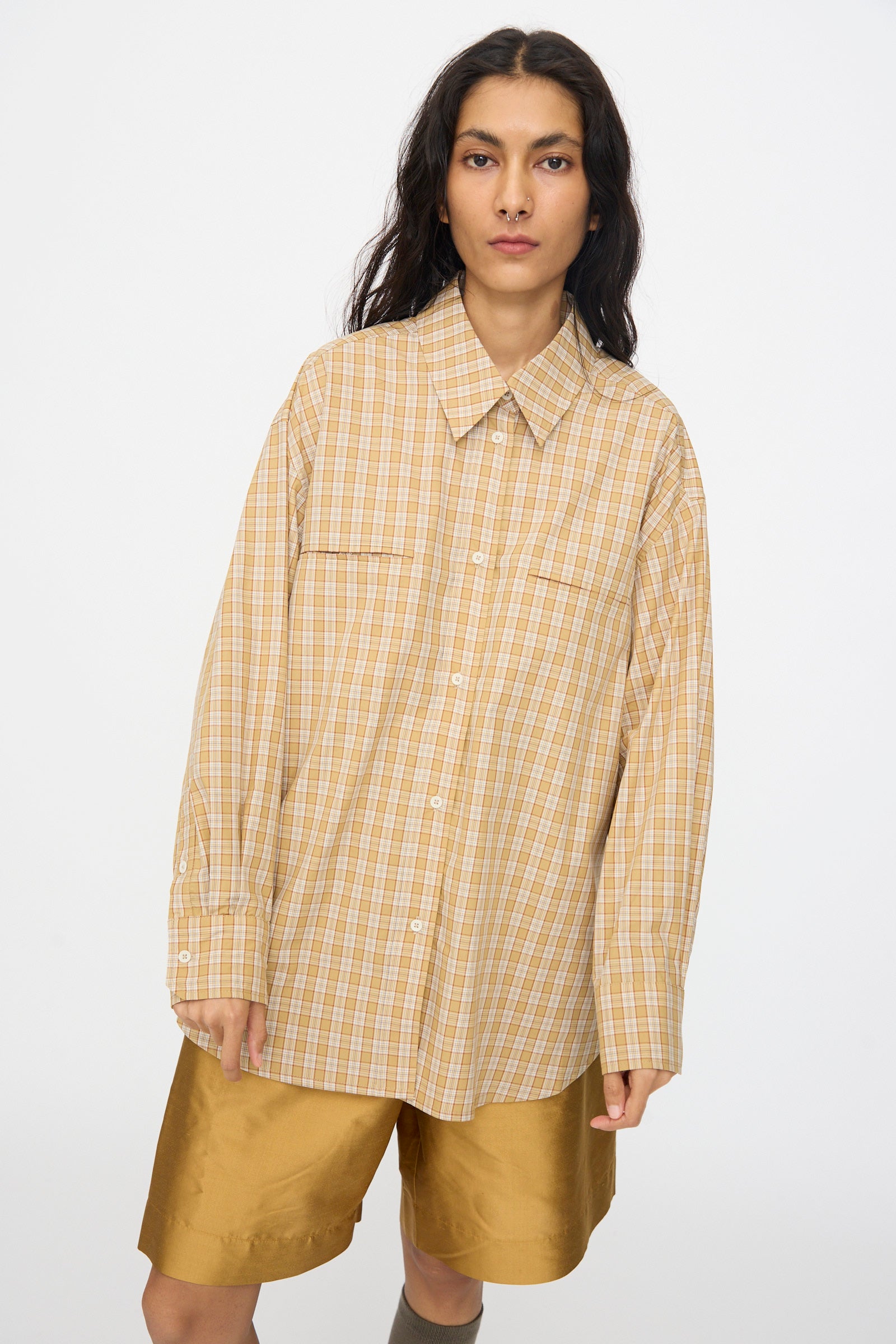 A person wearing the Cawley Checked Cotton Phoebe Shirt in Ochre, Red and Purple Check and tan shorts stands against a plain white background.