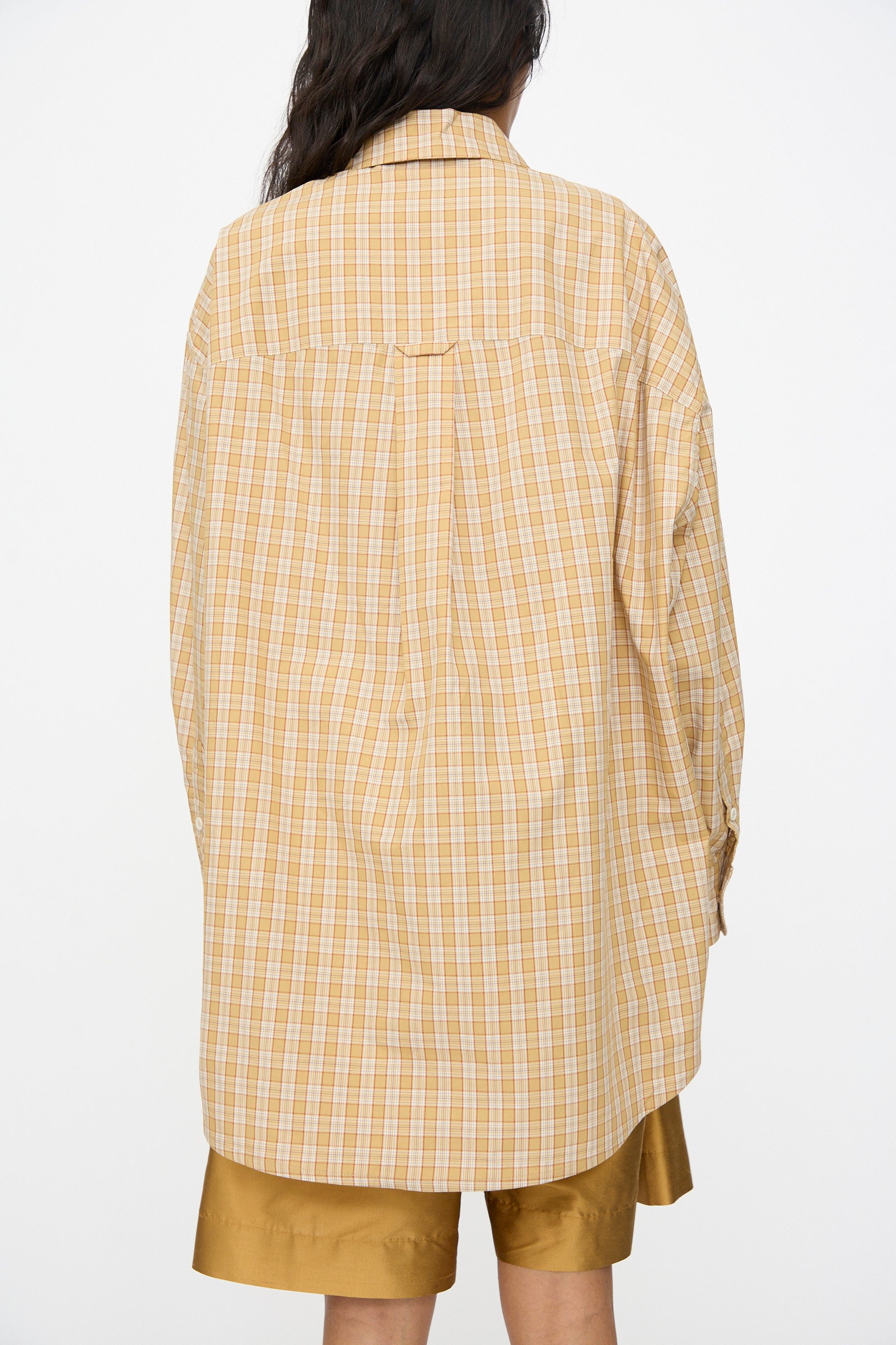 Model wearing the Cawley Checked Cotton Phoebe Shirt in ochre, red, and purple check, styled with tan shorts, shown from the back against a plain white background.