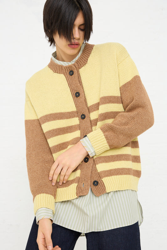 A person wearing a Cotton and Lambswool Textured Stripe Cardigan in Celery and Nutmeg by Cawley over a light blue and white striped cotton shirt.