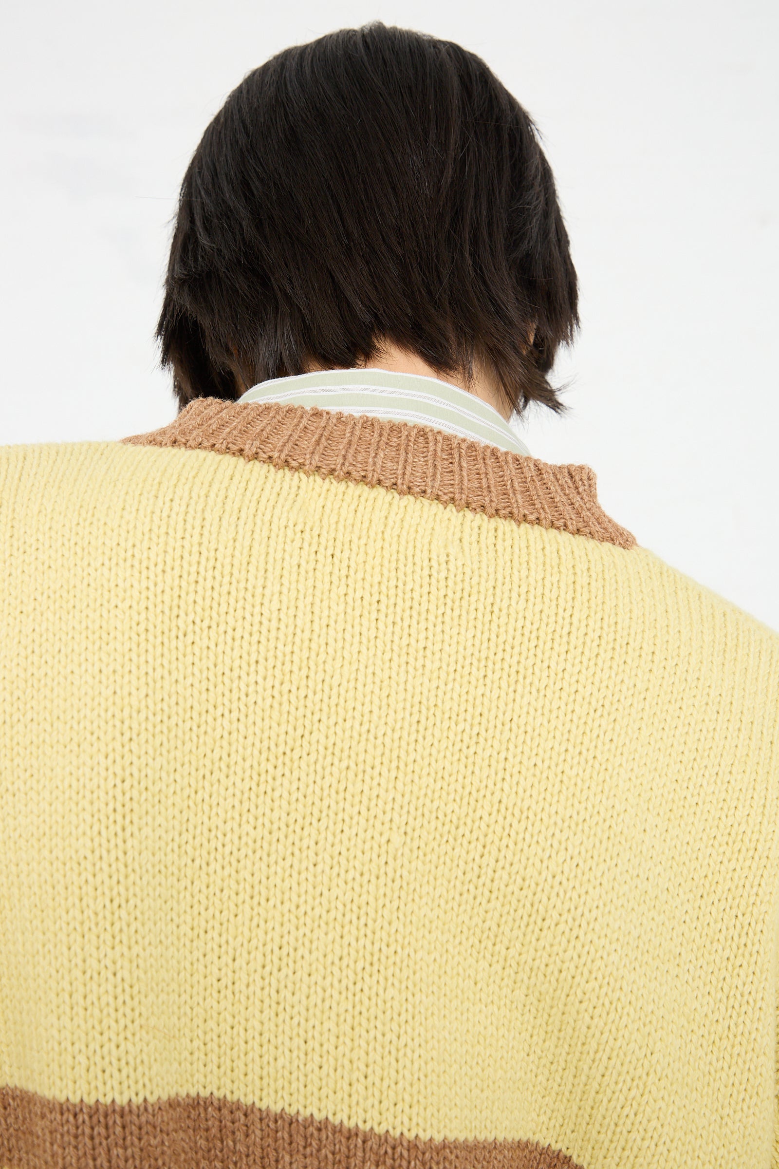 Person with dark hair wearing a yellow Cawley Lambswool sweater with brown stripes, viewed from behind.