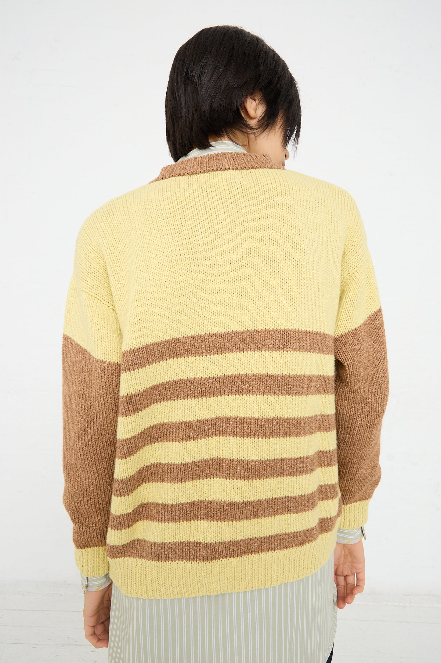 A person seen from behind wearing a Cawley Cotton and Lambswool Textured Stripe Cardigan in Celery and Nutmeg.